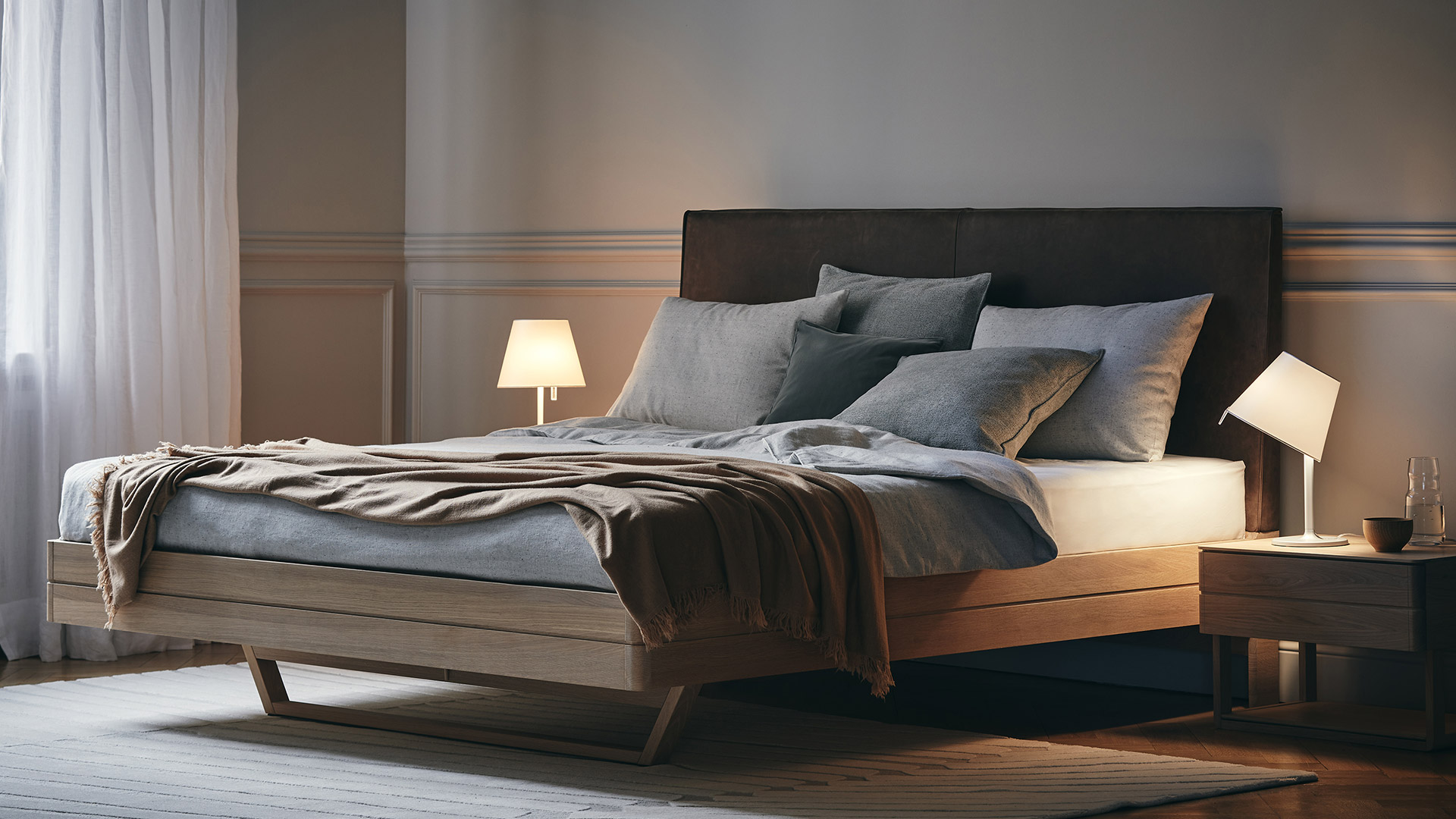 Artemide Melampo Tavolo table lamp with white conical shade on slim white stem, glowing warmly on a wooden desk