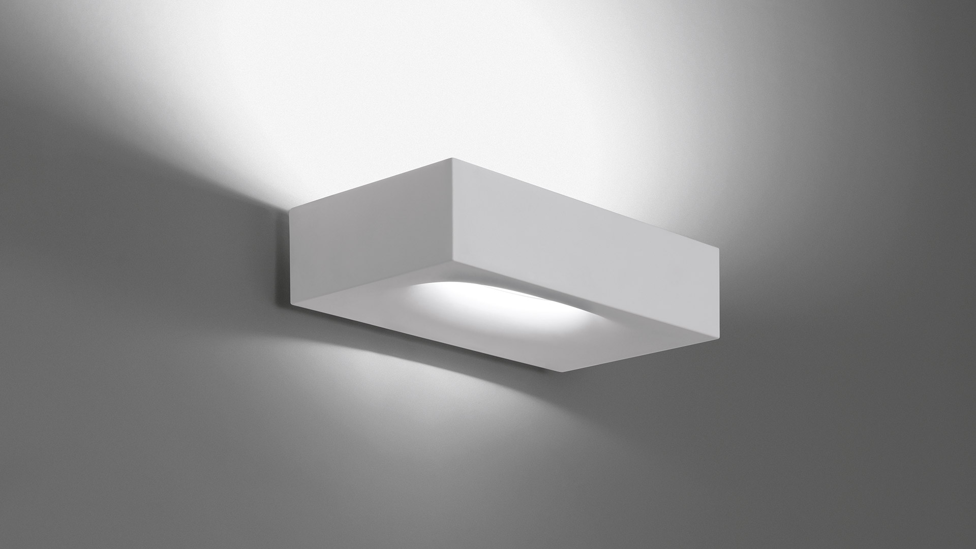 Artemide Melete wall lamp, white rectangular plaster body, emitting soft upward and downward light against a grey wall