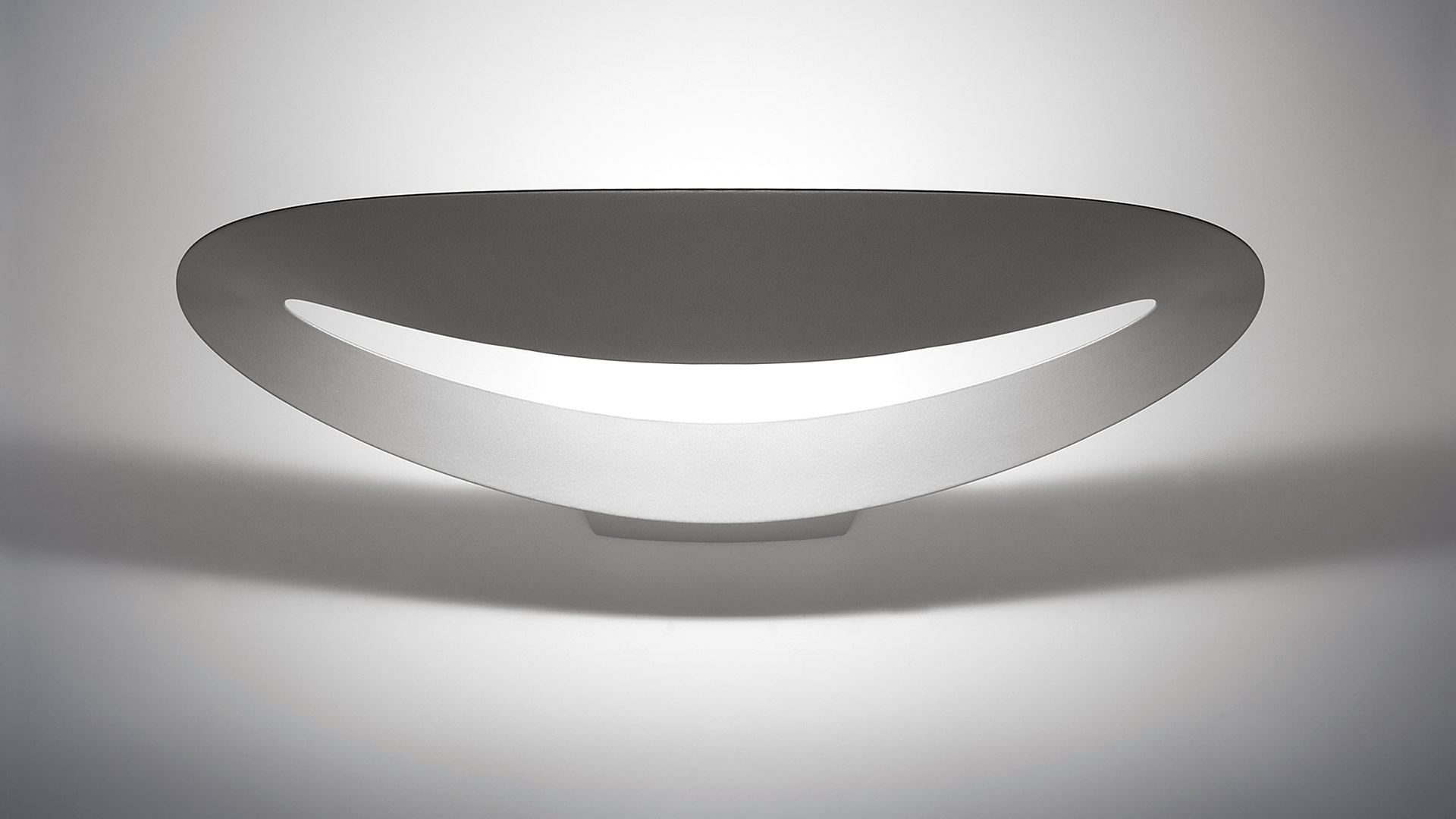 Artemide Mesmeri wall lamp: sleek oval white diffuser emitting soft indirect light through a curved bottom slit