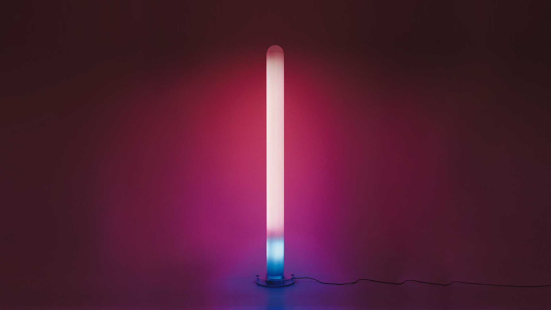 Artemide Metacolor floor lamp: tall cylindrical tube emitting gradient light from cyan base to pink-magenta top against dark background