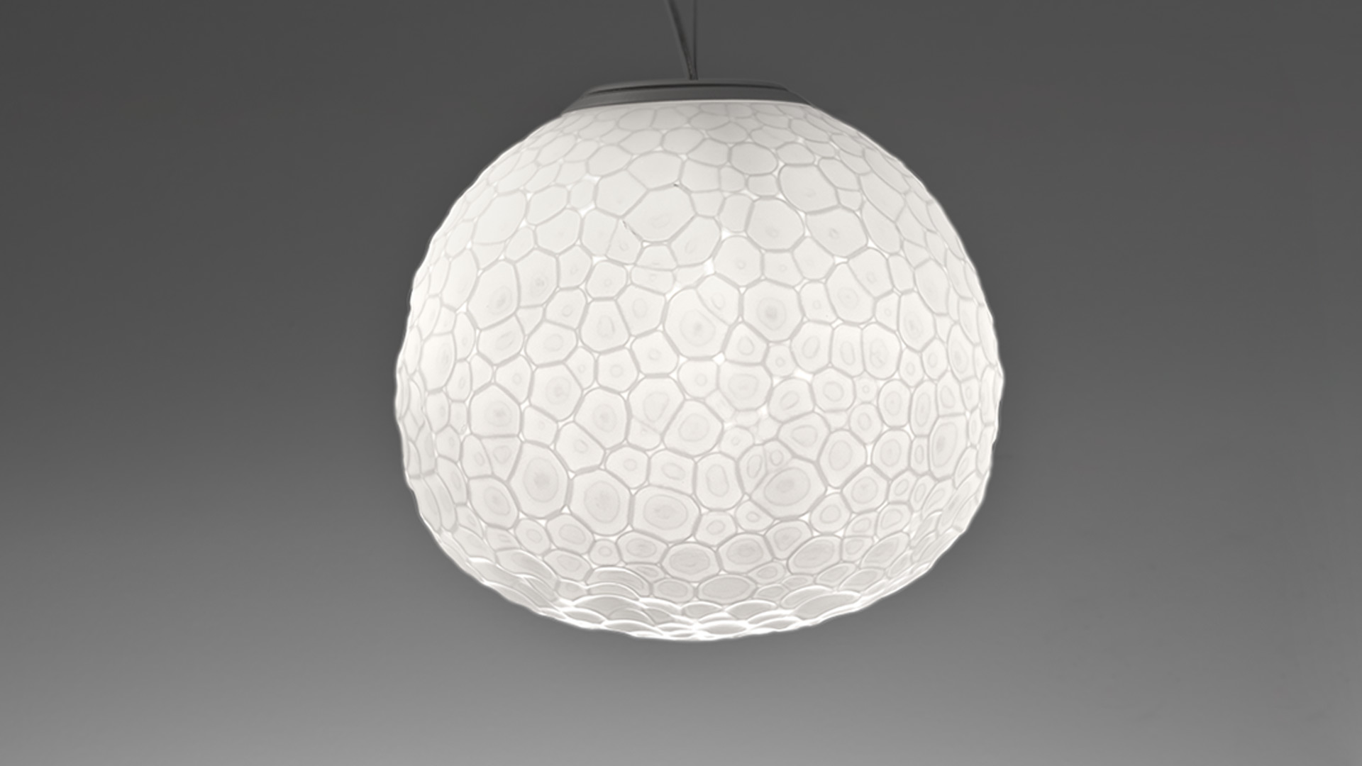 Artemide Meteorite suspension lamp: spherical white diffuser with crater-like texture, emitting warm ambient glow against dark background