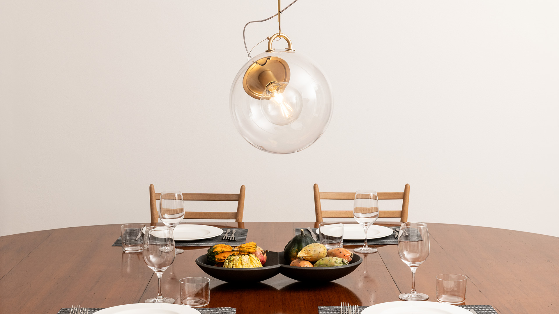 Artemide Miconos pendant lamp with clear glass globe and brass fitting, hanging over a wooden dining table set for four