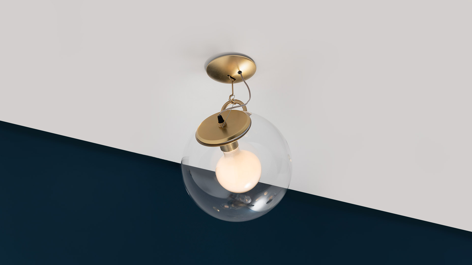 Artemide Miconos wall lamp with chrome arm and transparent glass sphere diffuser, emitting soft warm light against a grey wall