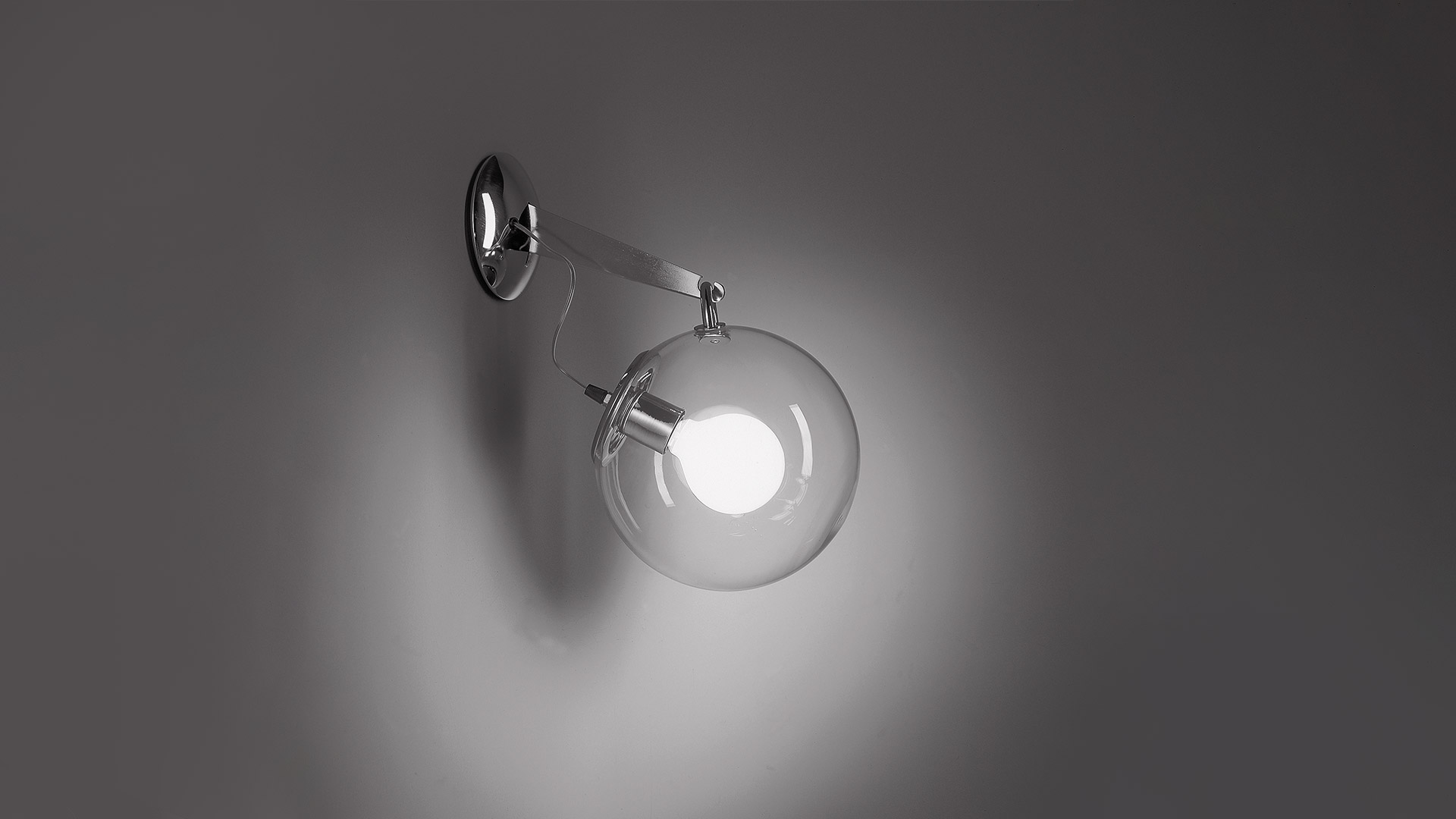 Artemide Miconos wall lamp with brushed brass arm and clear spherical glass globe shade, mounted on white wall