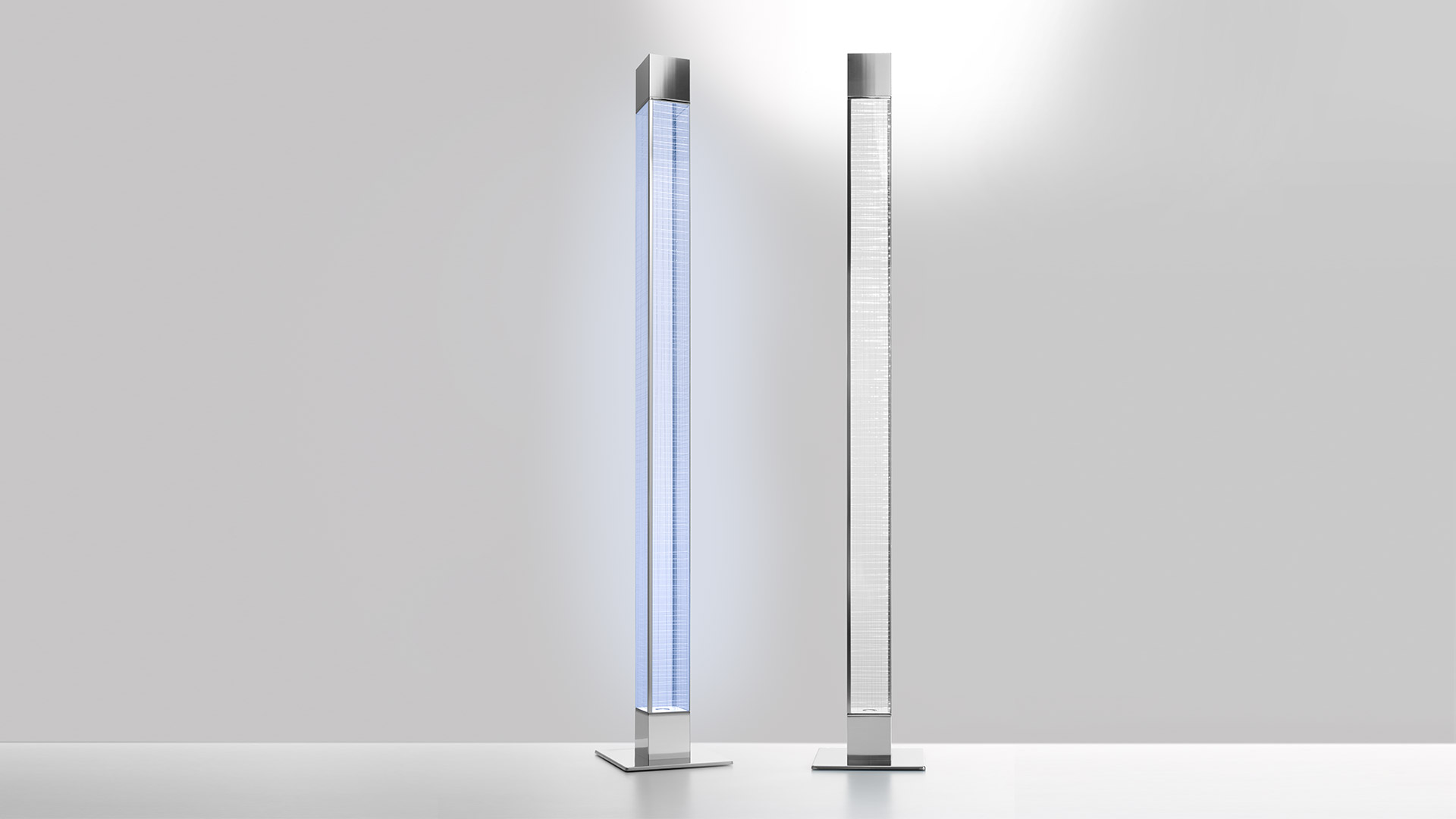 Two Artemide Mimesi floor lamps: left emitting blue light through glass column, right glowing white, both on square metal bases