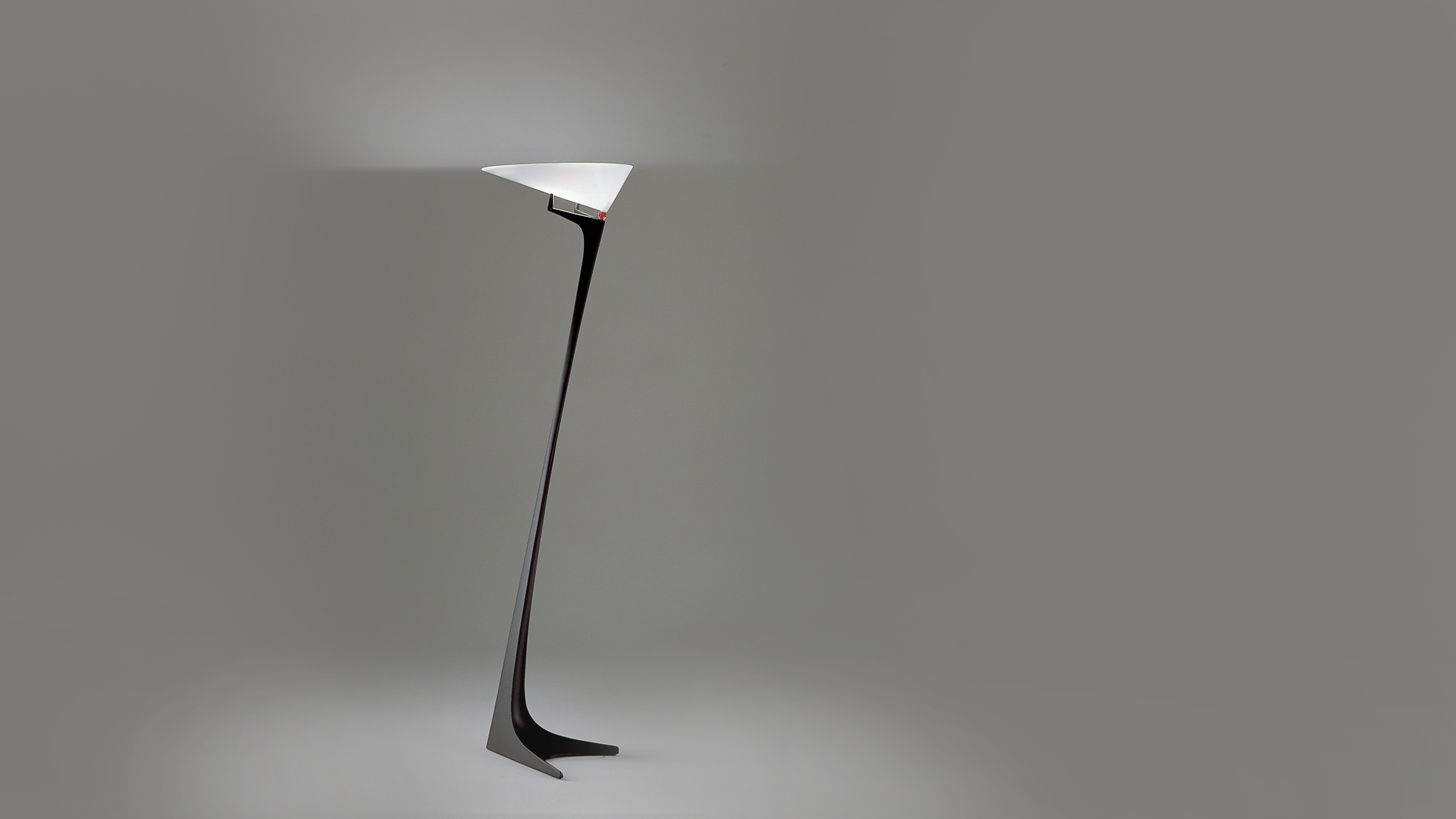 Artemide Montjuic floor lamp with sleek black sculptural base and triangular white diffuser emitting upward indirect light