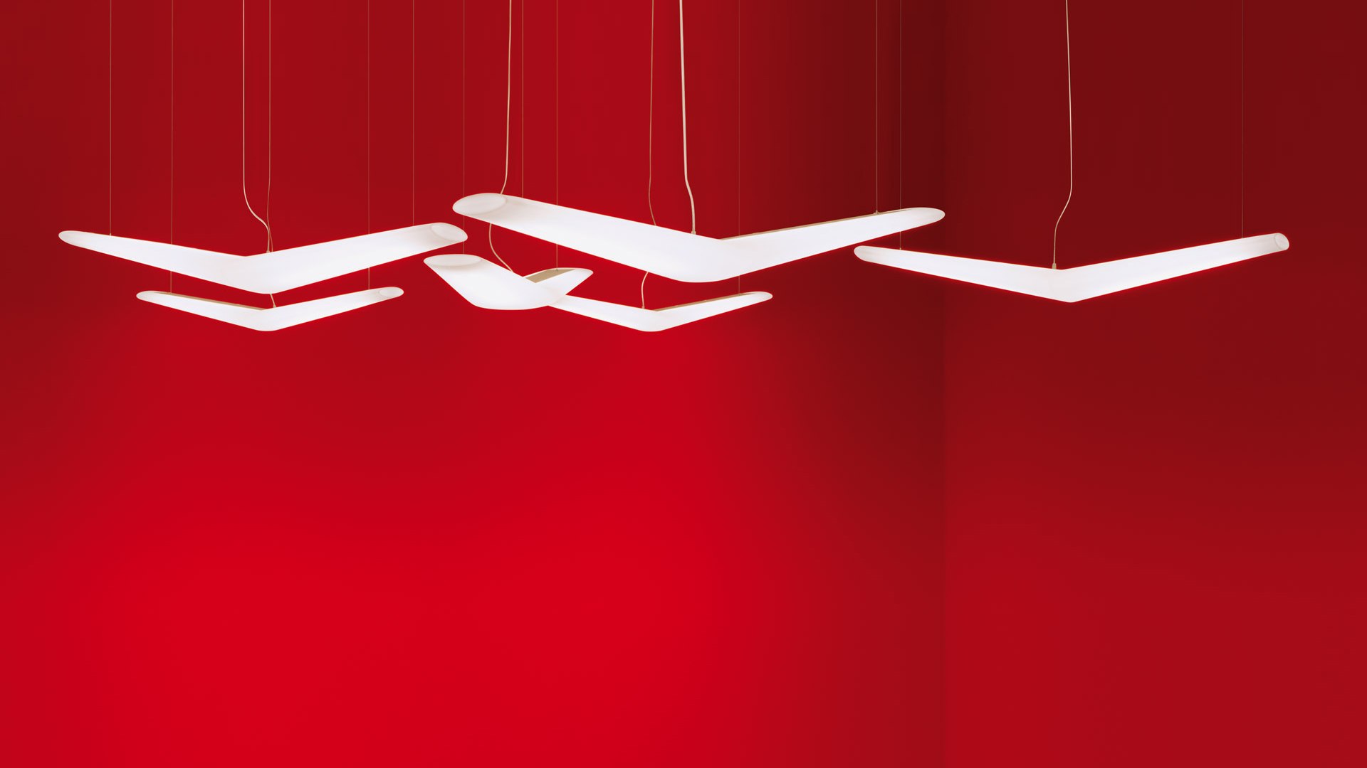 Three Artemide Mouette pendant lamps with white wing-shaped diffusers suspended by thin cords against a red background
