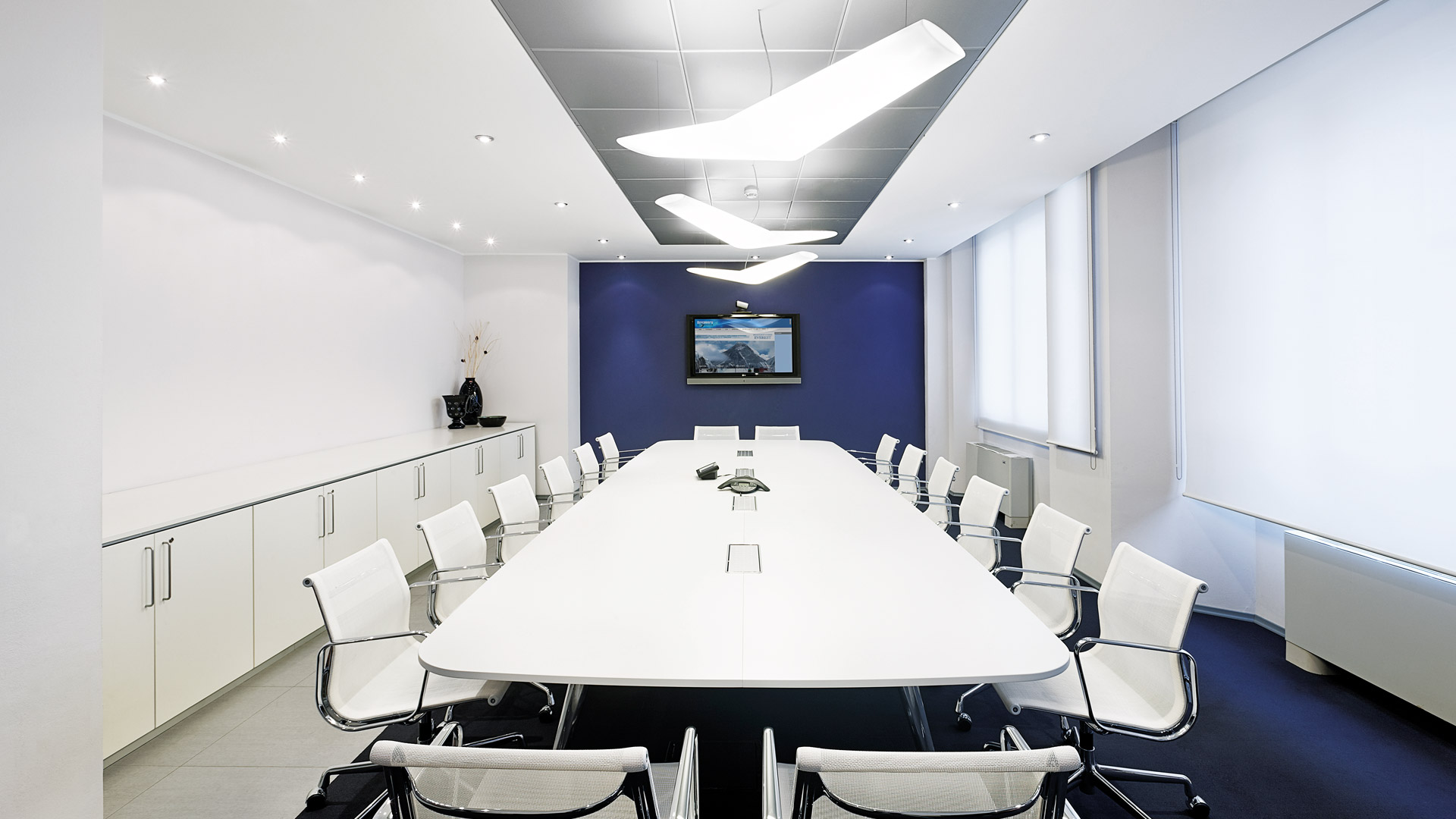 Modern conference room with Artemide Mouette pendant lamps above a long white table surrounded by white chairs, blue accent wall.