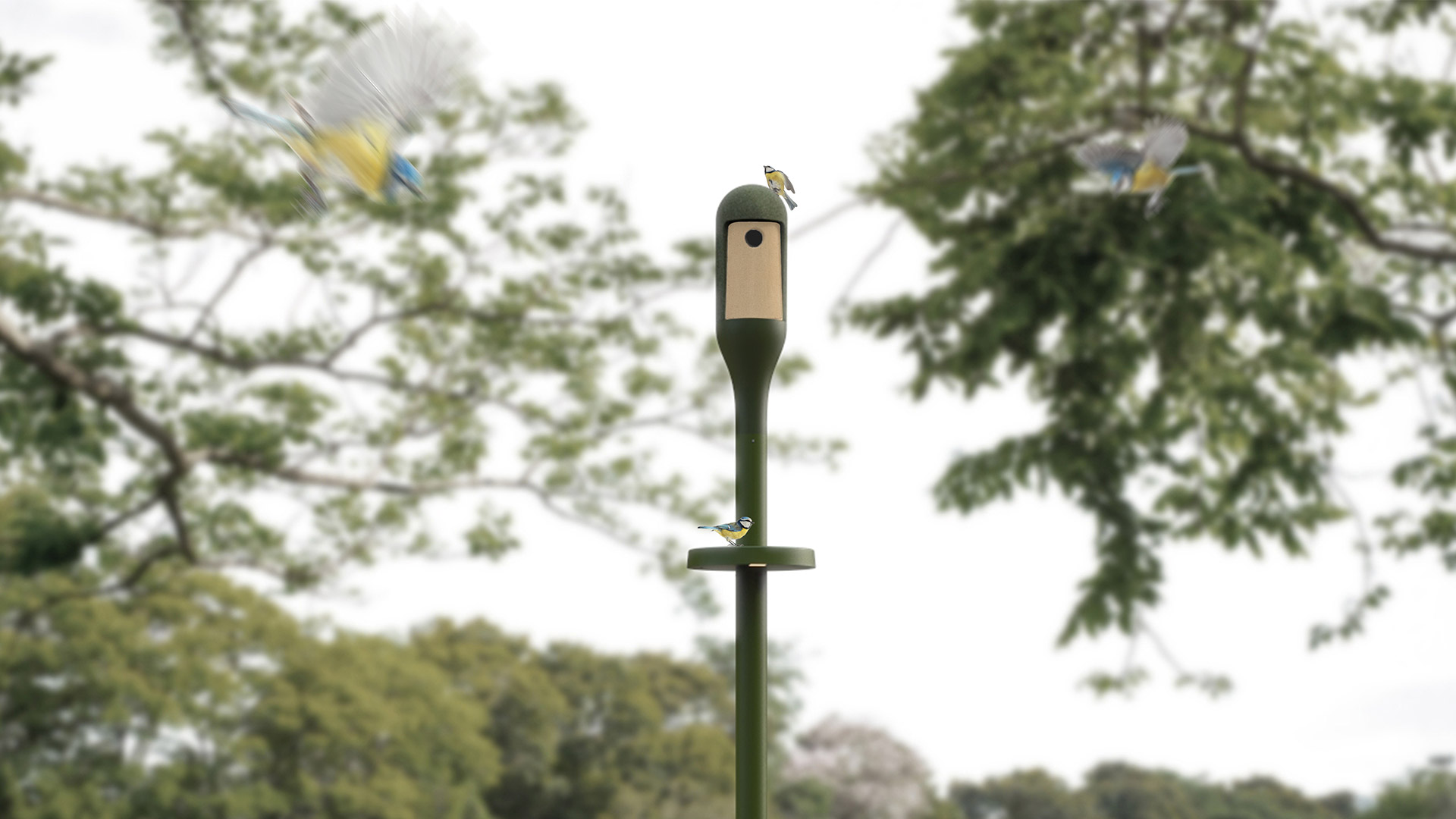 Needoo outdoor lamp by Artemide: dark green pole with birdhouse-shaped luminaire head, installed in a garden with trees