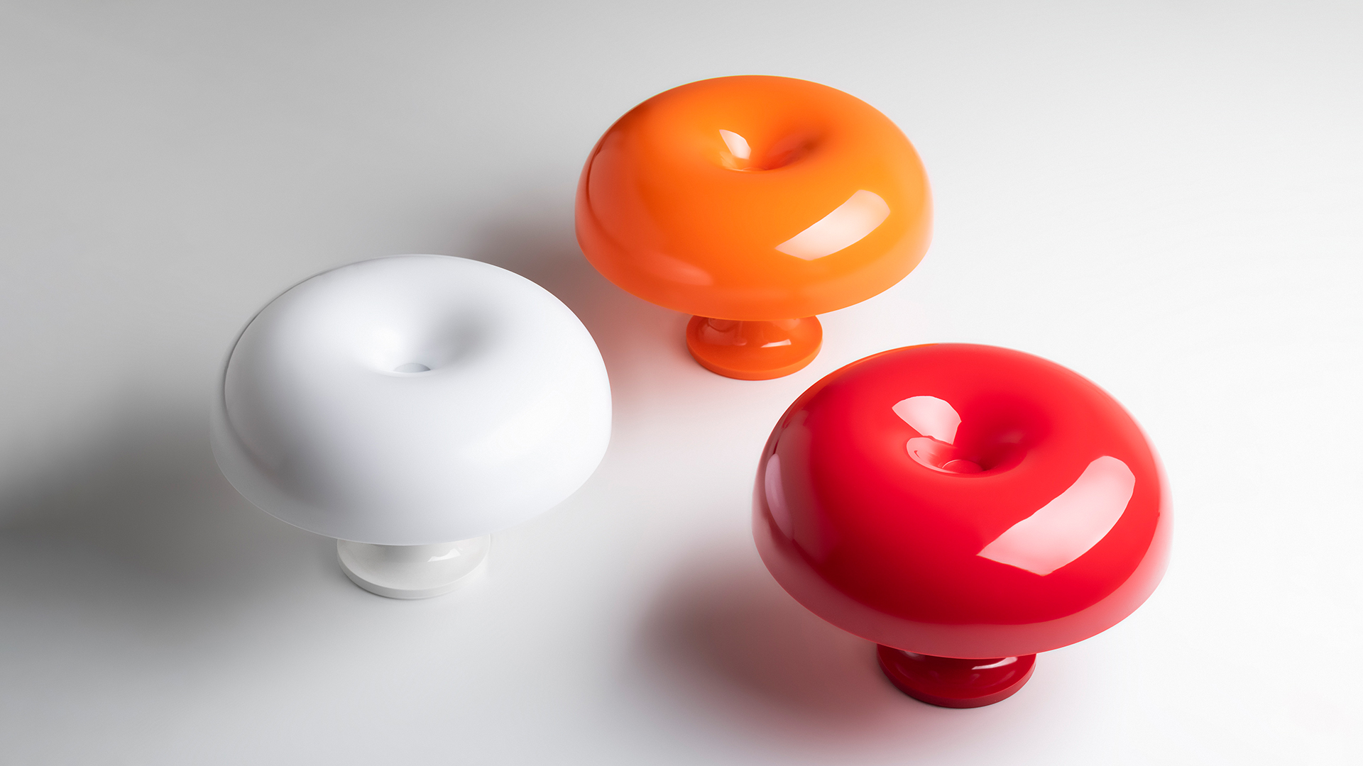 Artemide Nessino table lamp in deep red, featuring iconic donut-shaped shade on pedestal base, shown alongside matching red design objects