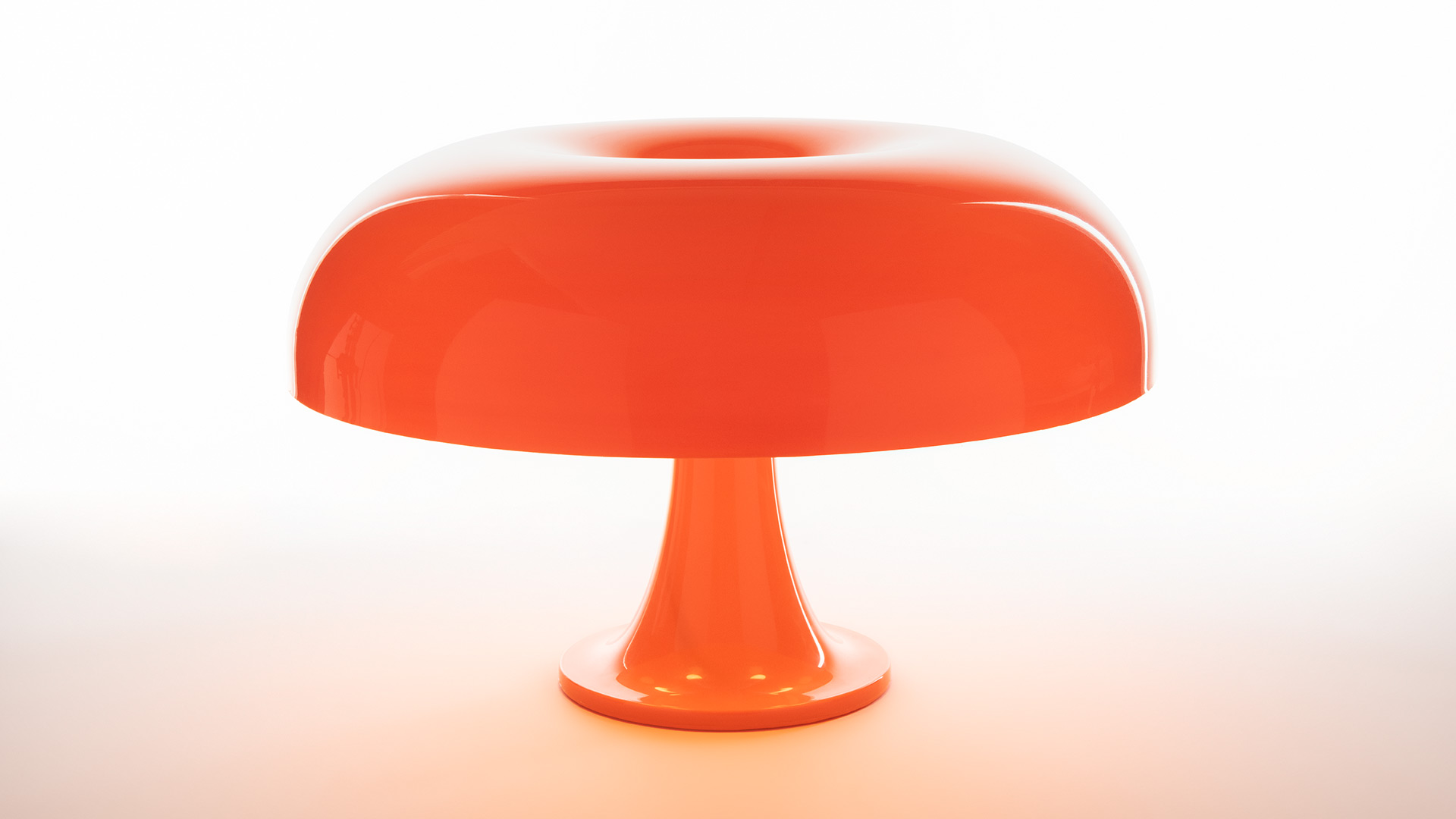 Two Artemide Nesso table lamps in deep red, mushroom-shaped design, displayed on sculptural red pedestals against velvet curtains
