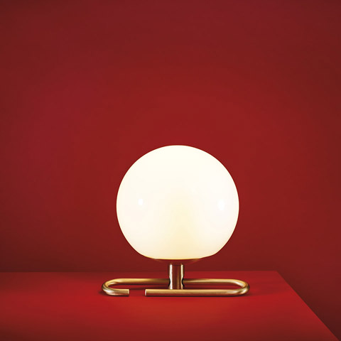 Artemide NH1217 table lamp: glowing opal white glass sphere on a minimalist brushed brass rectangular base, against red background