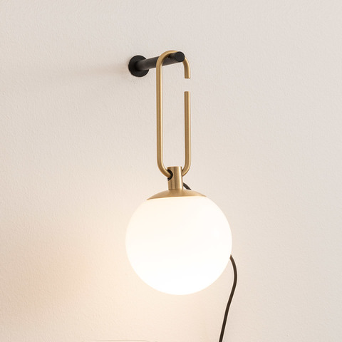 Artemide NH Parete wall lamp: brass oval hook bracket on black wall mount, suspending a frosted white glass globe shade with black cord