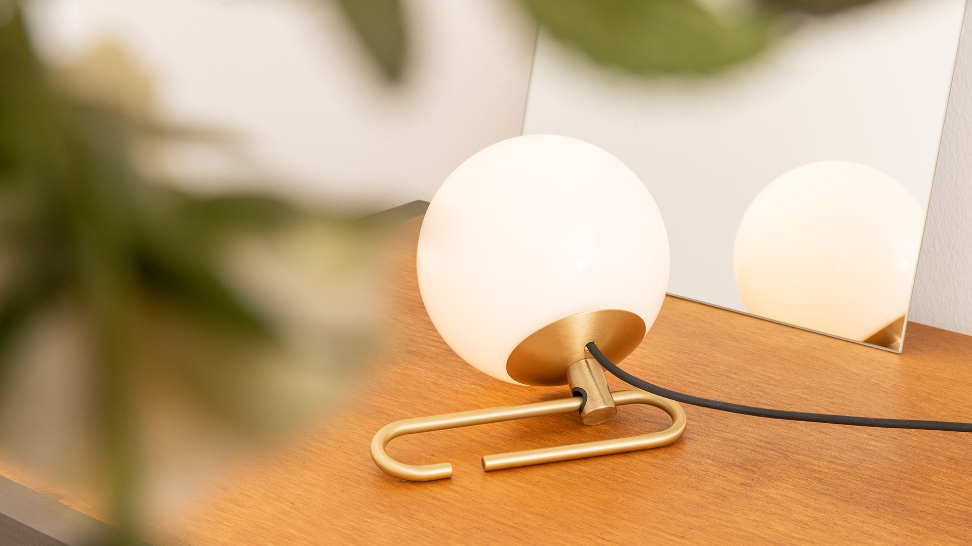 Artemide NH1217 table lamp: opal white glass sphere on a curved brass tubular base, displayed against a red background