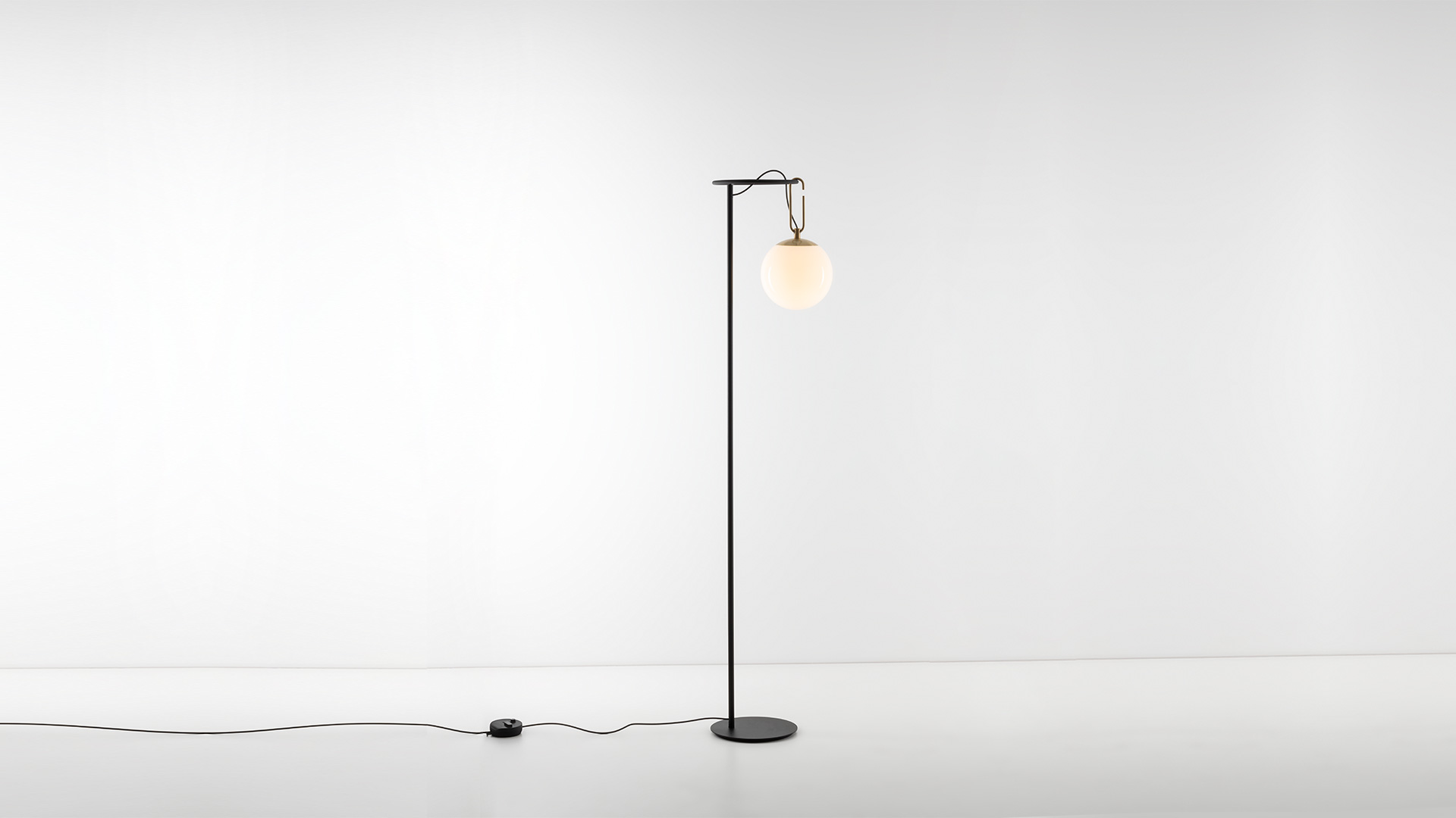 Artemide NH Terra floor lamp: tall black metal stem with circular base, opal glass globe shade suspended by a brass hook
