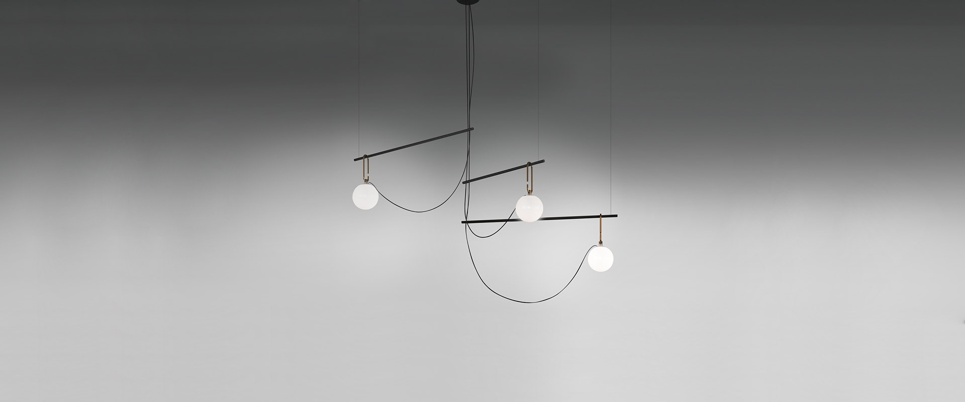 Three Artemide NH pendant/ceiling lamps with opal white glass globes of varying sizes, suspended by brass links from black ceiling mounts