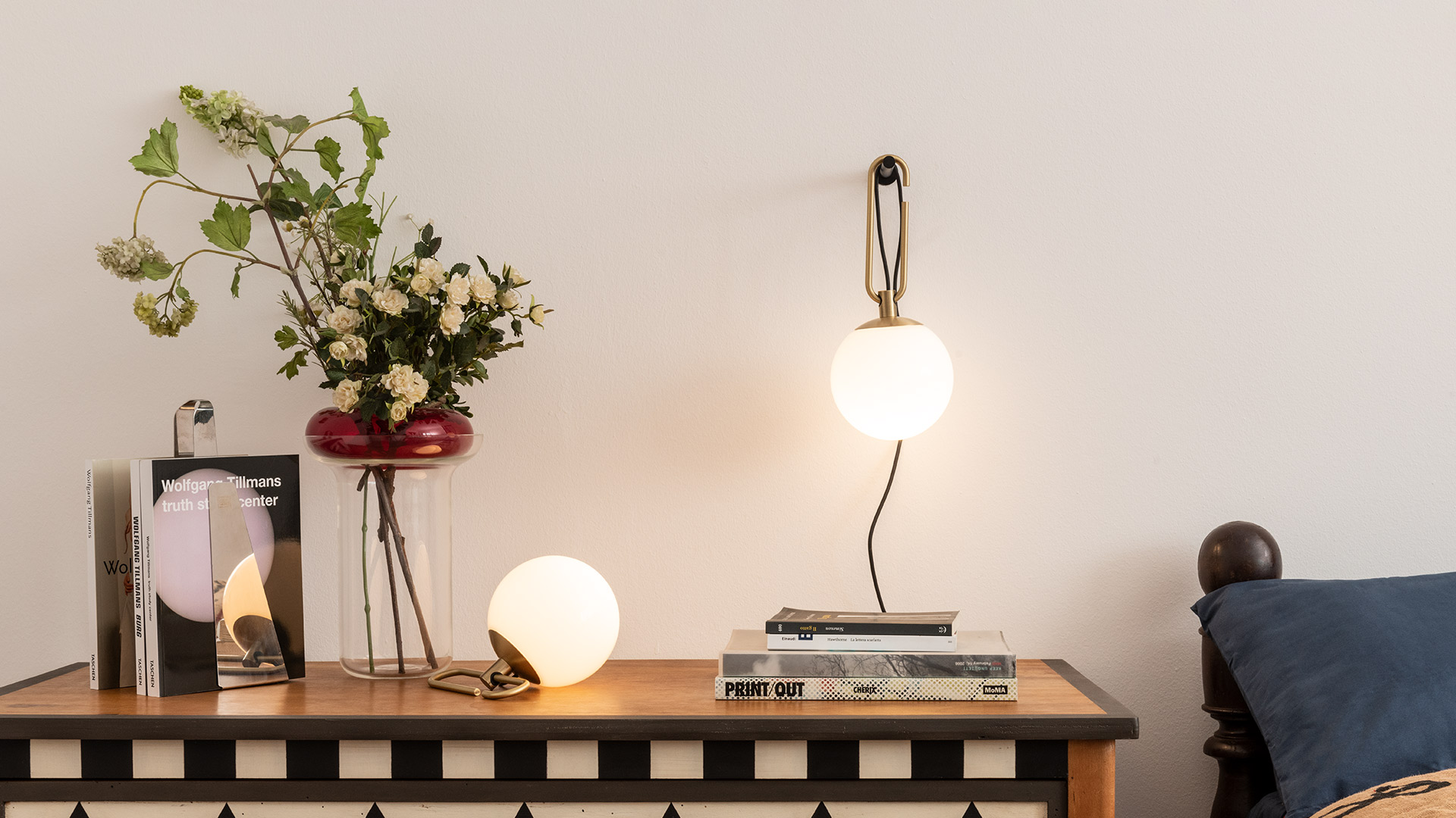 Artemide NH1217 table lamp: opal white glass sphere on brushed brass base with J-shaped hook, black cable, reflected in mirror