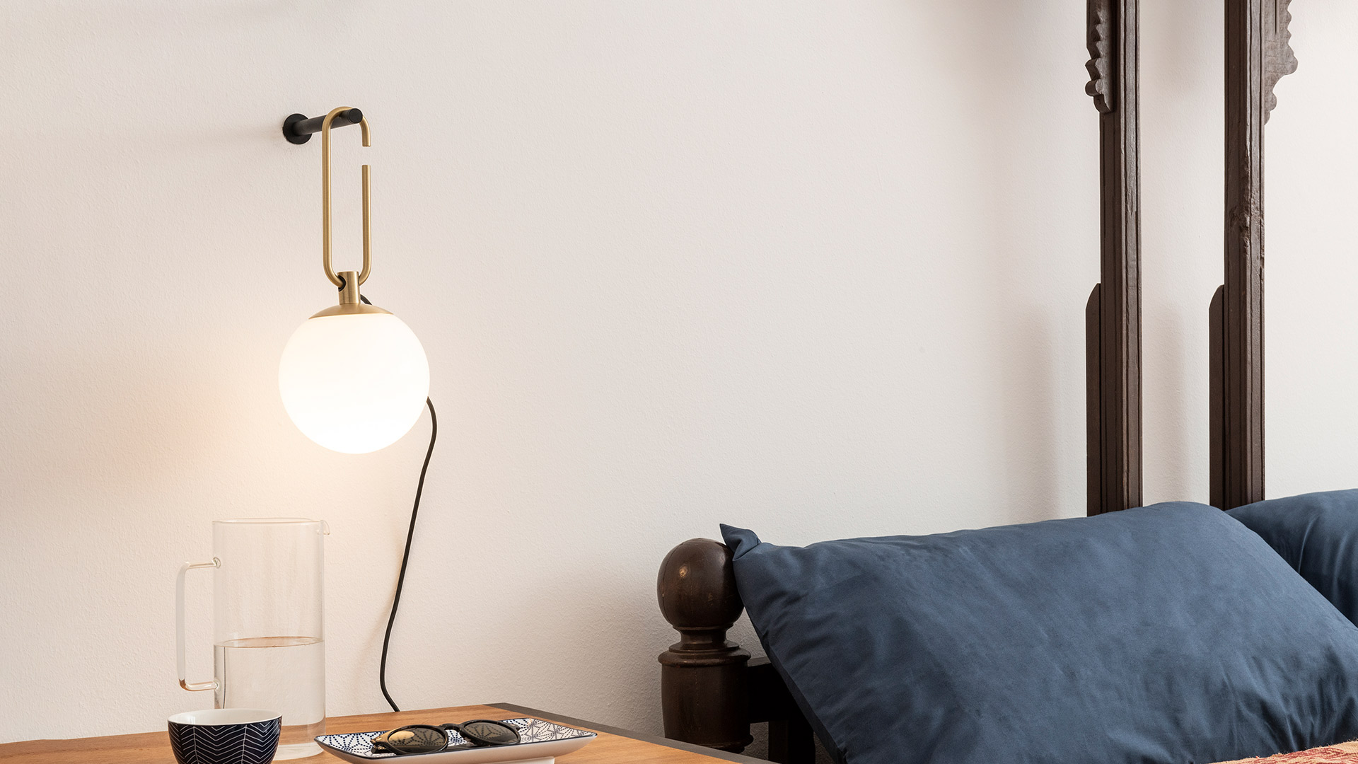 Artemide NH table lamp with opal glass sphere on dresser, and NH Parete wall lamp with brass hook above stacked books