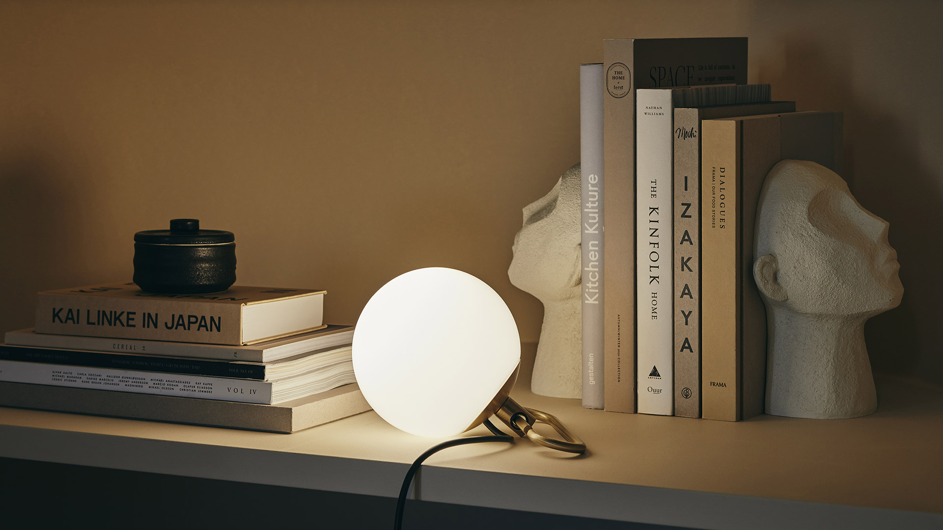Person on a library ladder reading a book, illuminated by two Artemide NH table lamps casting warm focused light on bookshelves