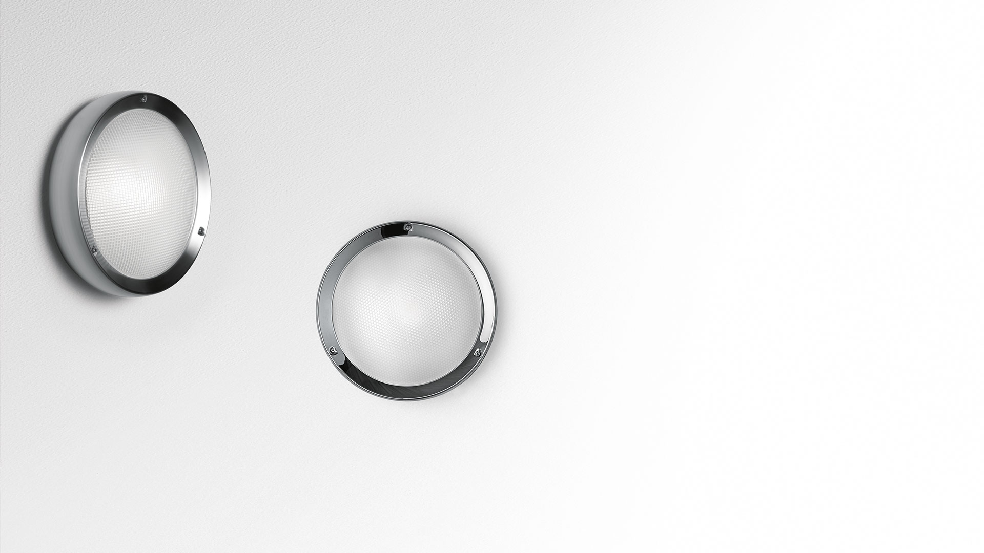 Two Artemide Niki wall lights with circular chrome frames and frosted glass diffusers, mounted on a white wall