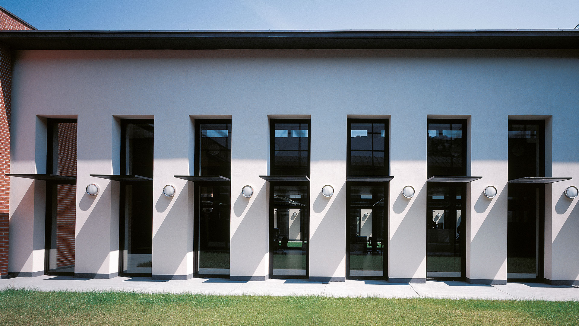 Modern building facade with tall dark-framed windows and Artemide Niki wall sconces mounted between each window bay