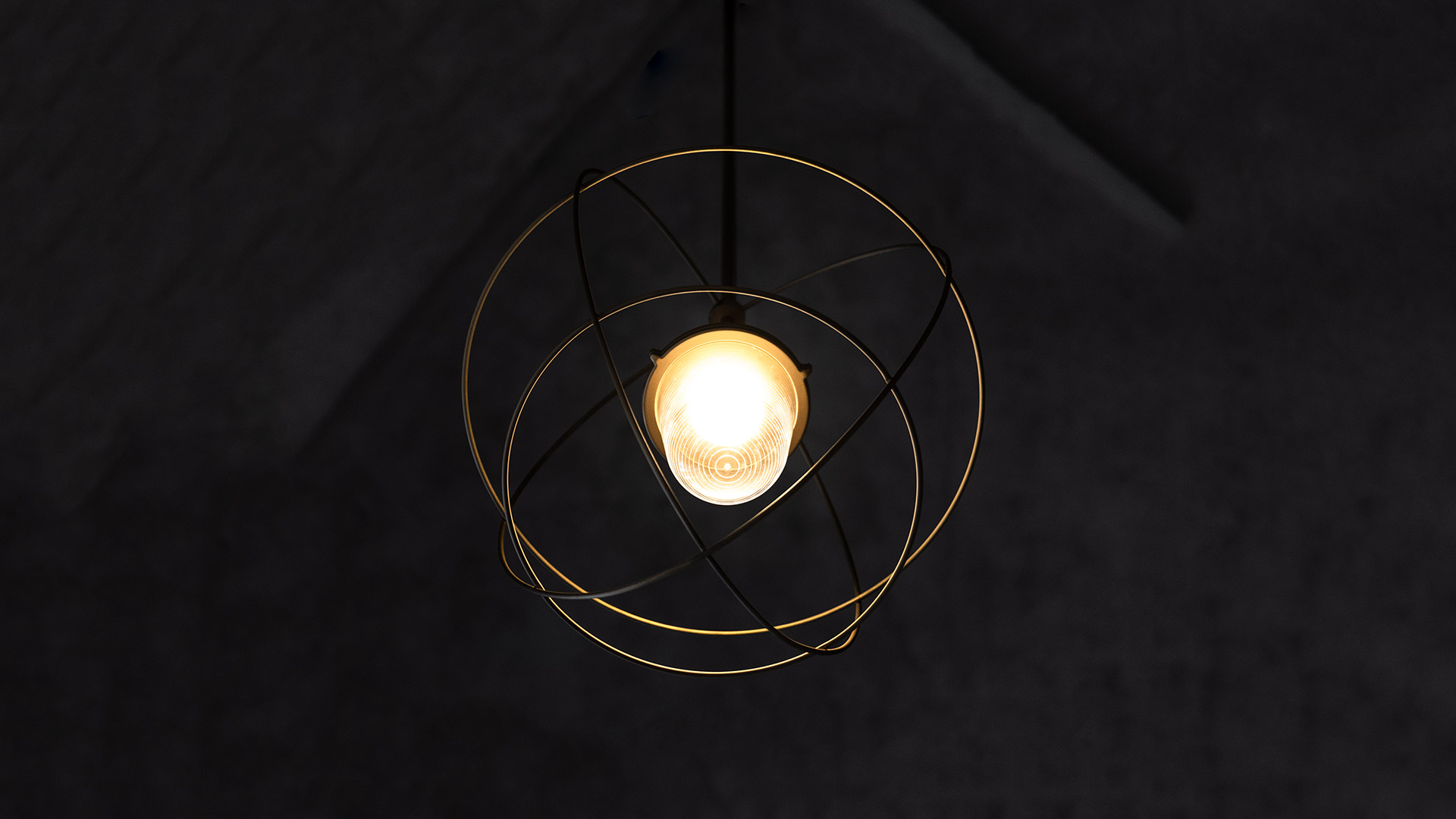 Artemide Nottola pendant lamp: exposed bulb encased in intersecting golden metal rings, suspended against a dark ceiling