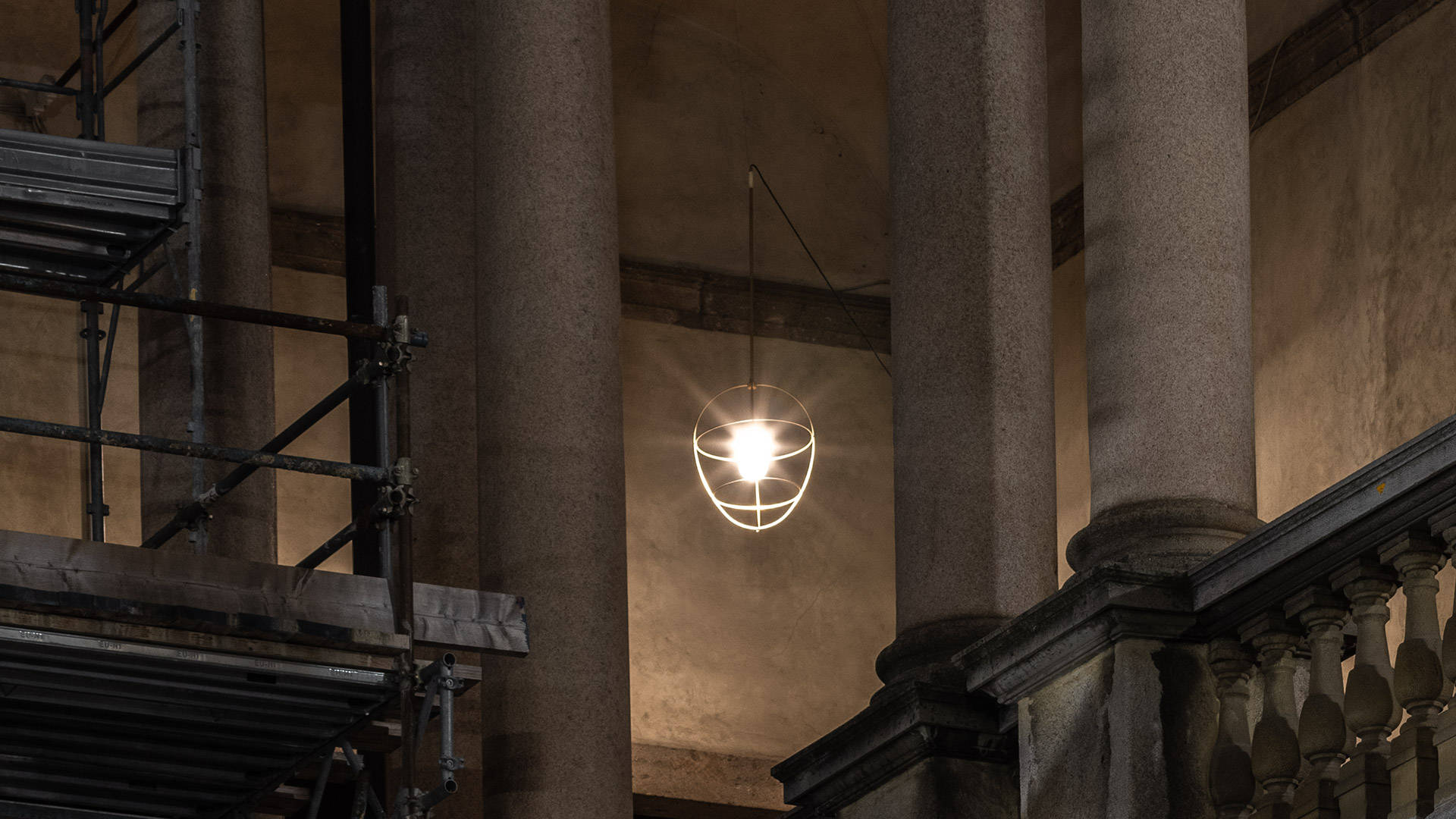 Artemide Nottola pendant lamp with white cage frame and exposed bulb, hanging between classical stone columns in a historic building