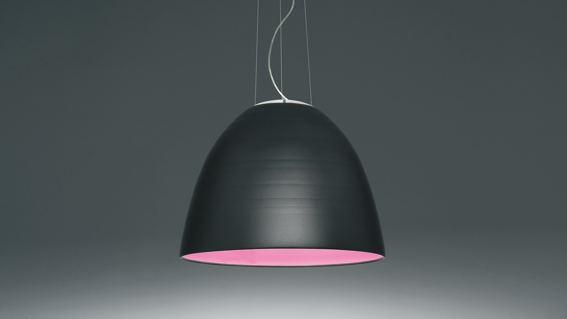 Three Artemide Nur pendant lamps in matte black with warm golden interior, hanging at varying heights on thin cables