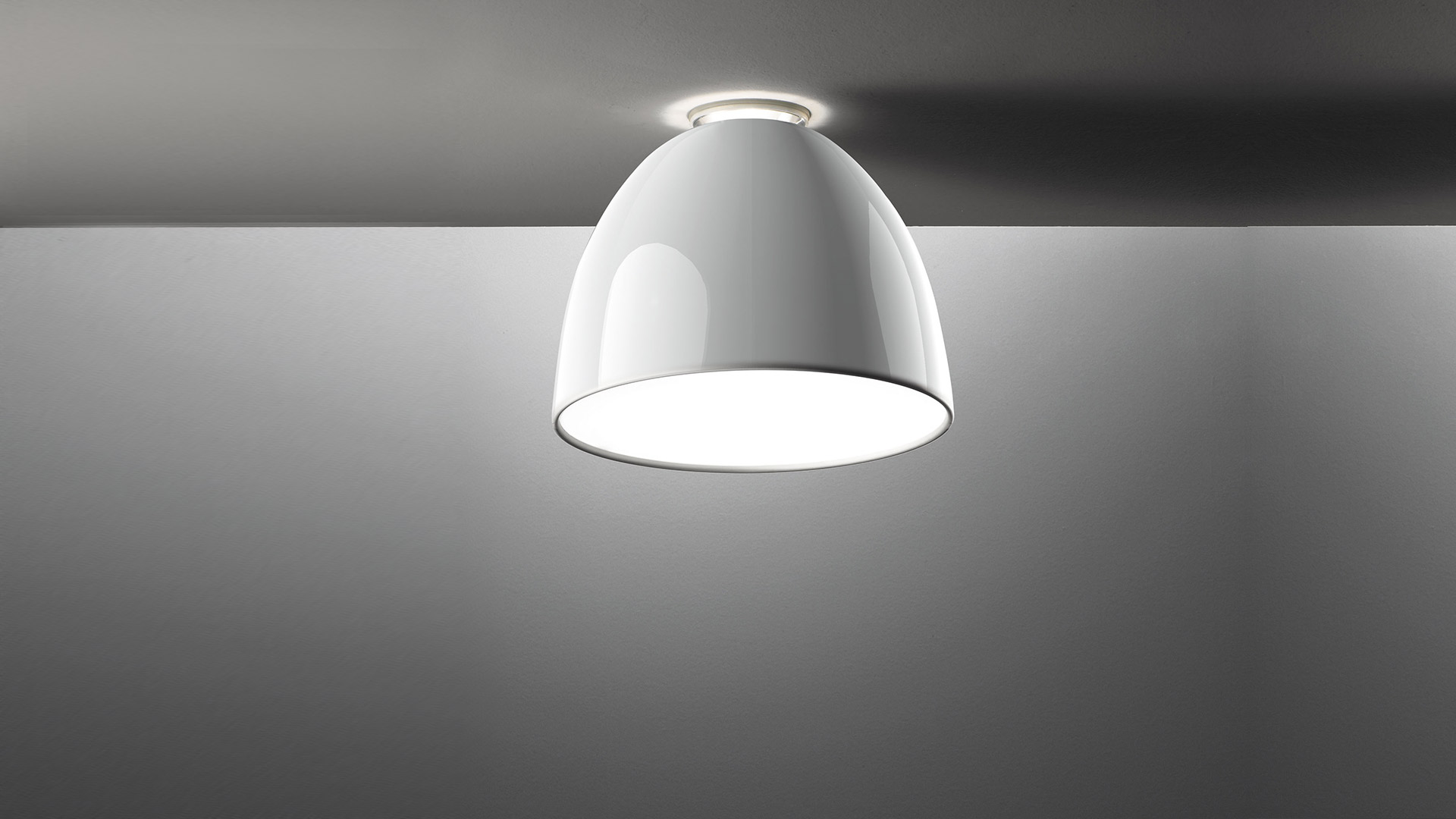 Artemide Nur Mini Gloss ceiling lamp with glossy white dome shade, flush-mounted on ceiling, emitting warm diffused light