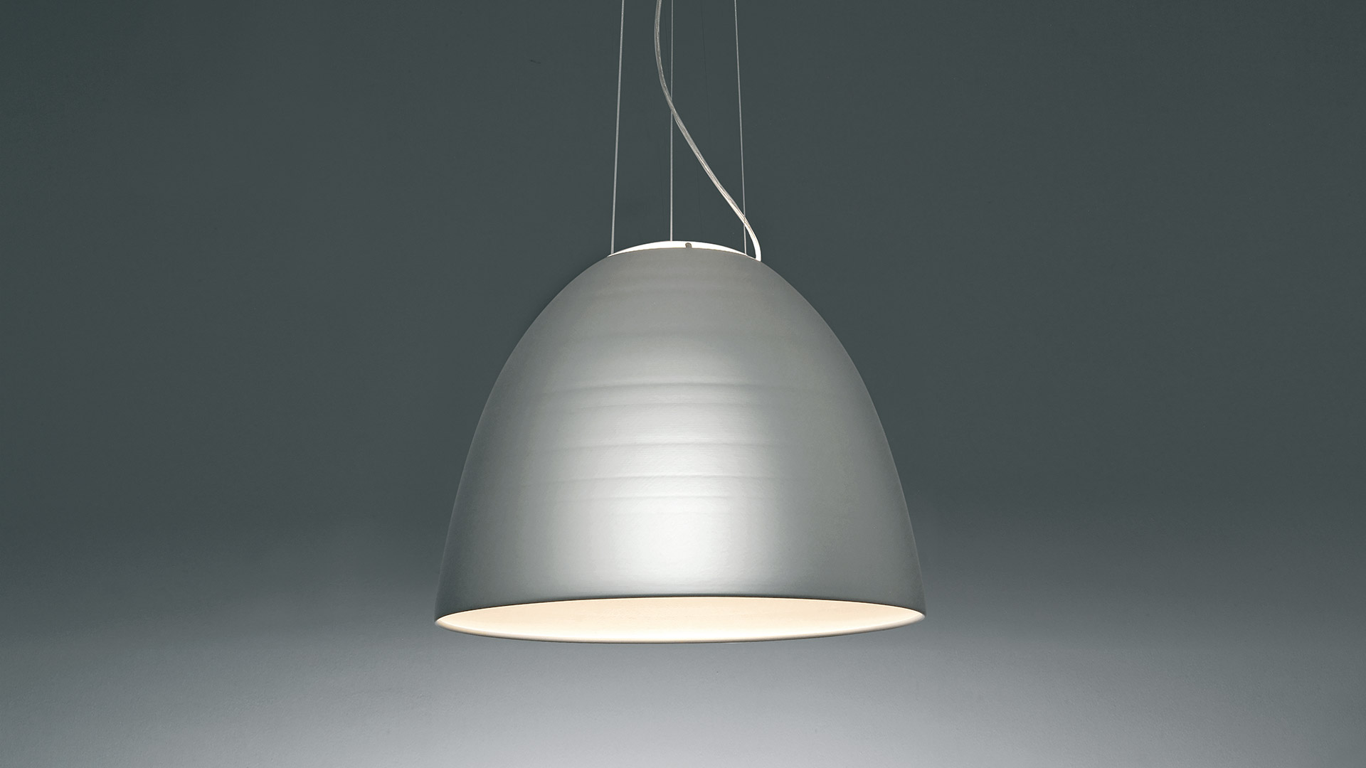 Artemide Nur pendant lamp with dark anthracite dome-shaped shade, white interior, suspended by thin cables on grey background