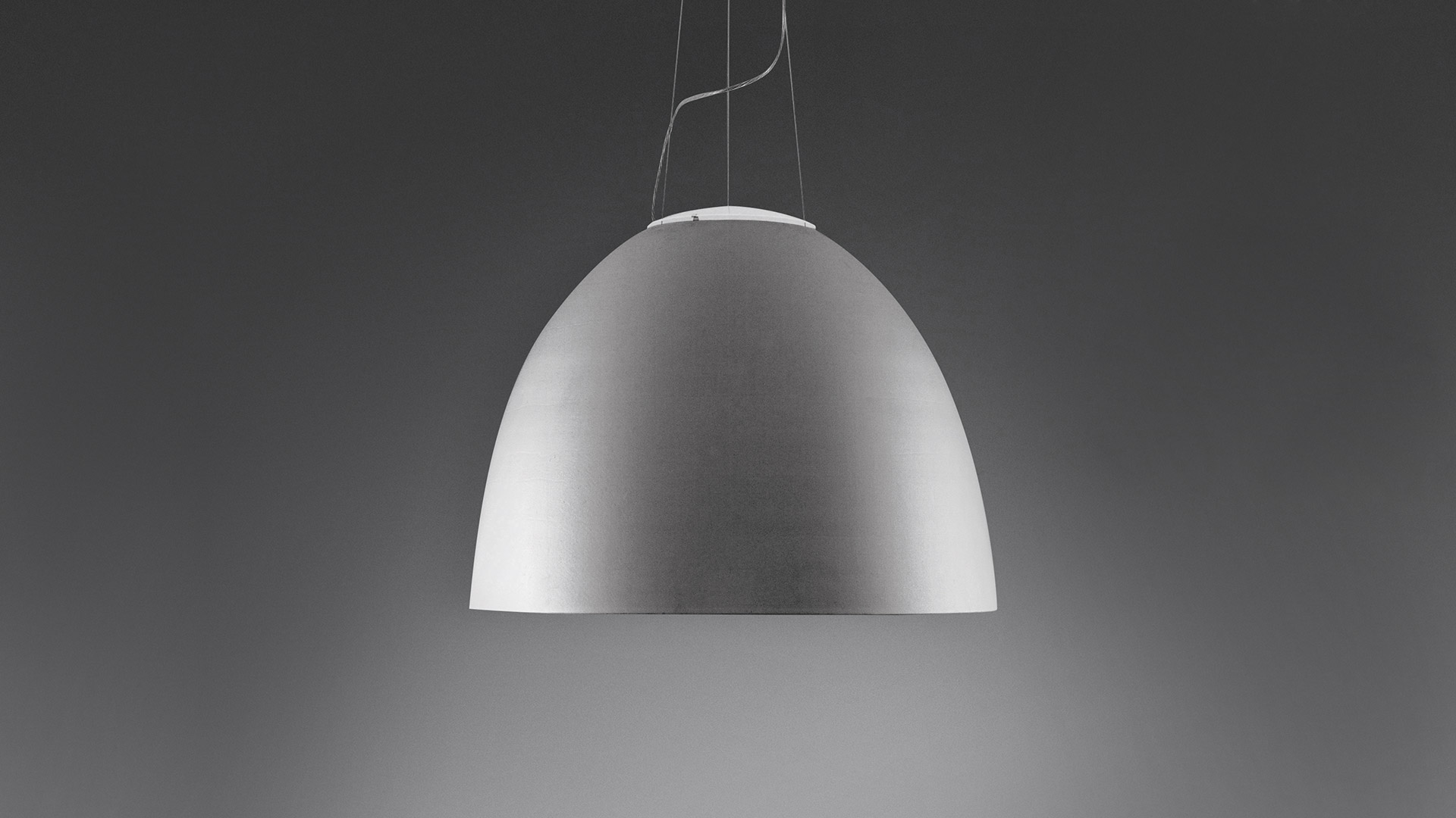 Three Artemide Nur 1618 pendant lamps in matte black with warm gold interior, hanging at varying heights on thin cables