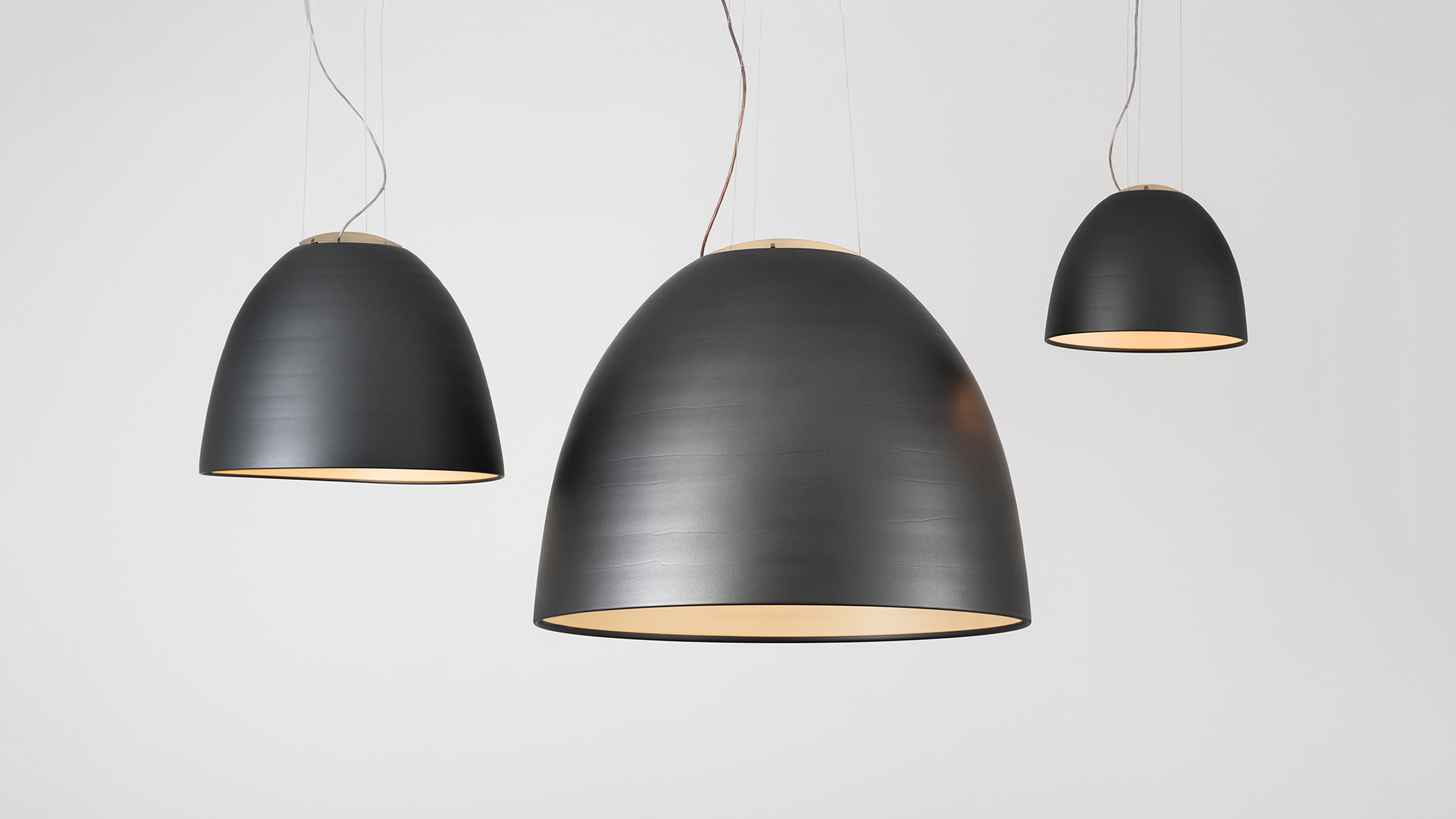Artemide Nur pendant lamp with dark anthracite dome shade and vibrant pink interior, suspended by white cables