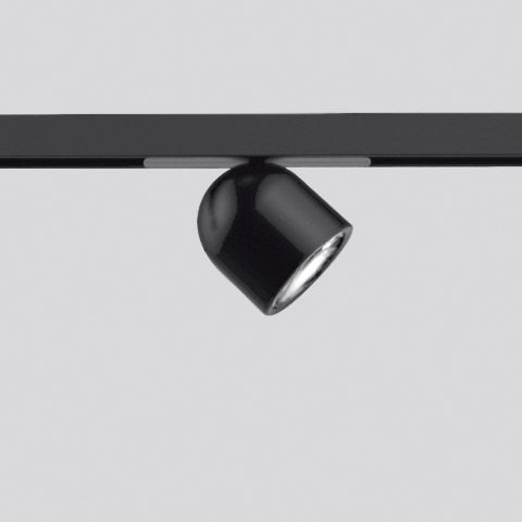 Artemide Olmo Spot: compact black track spotlight with rounded head, mounted on a black rail system, tilted at an angle.