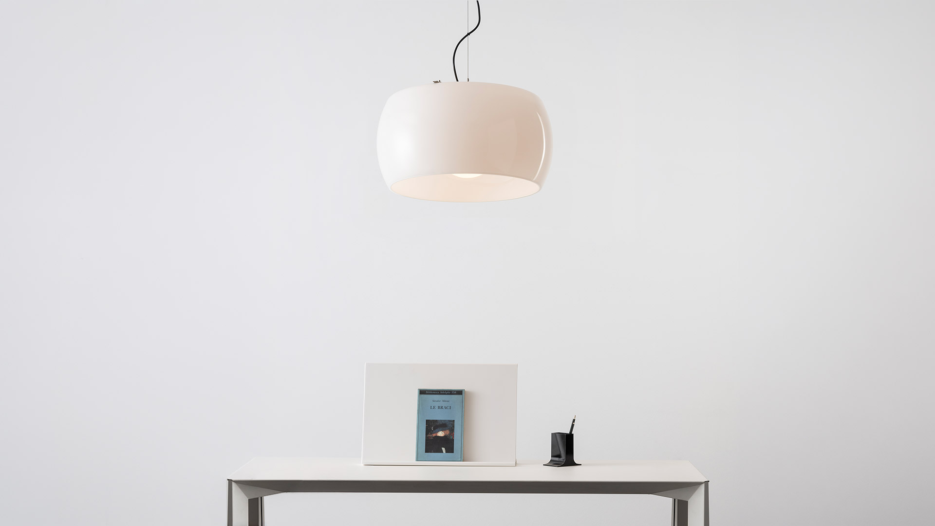 Artemide Omega pendant lamp with white opal glass shade hanging above a dark table with a decorative floral arrangement