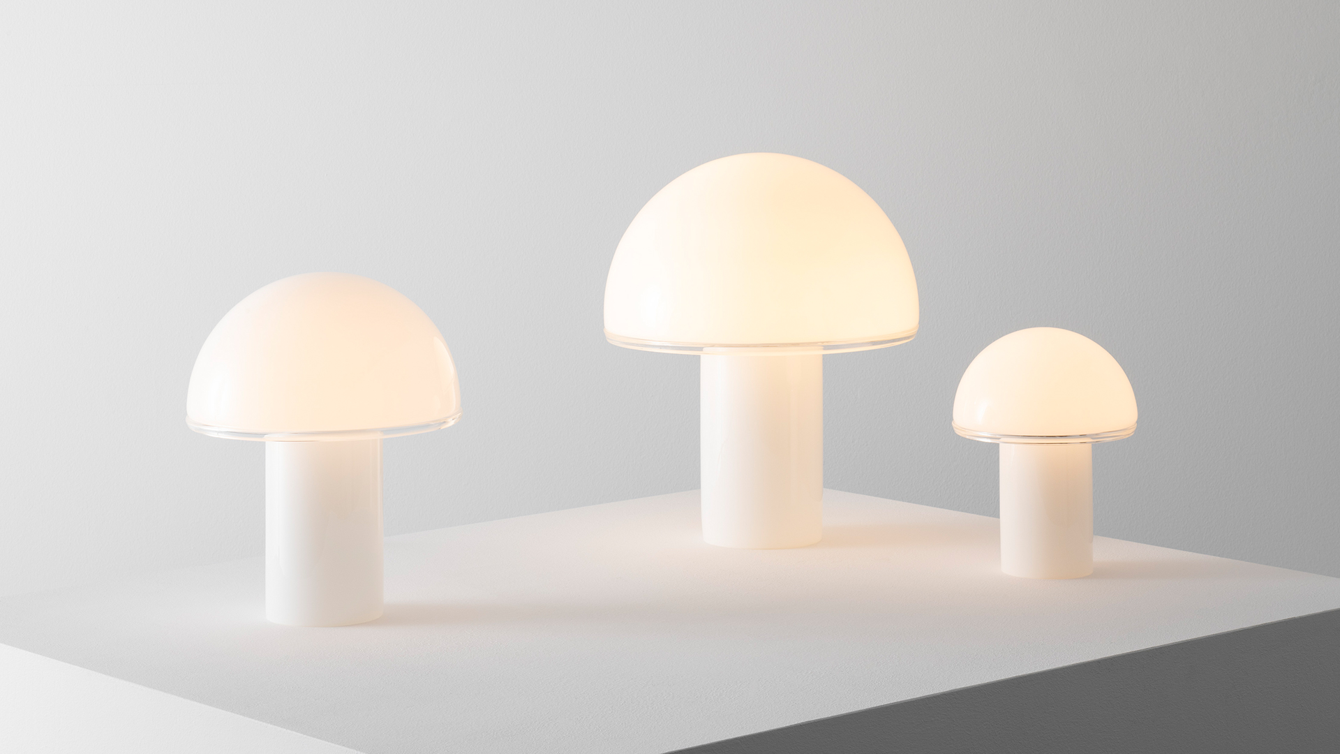 Artemide Onfale table lamp with white opal glass mushroom shade glowing warmly on a sideboard, next to framed artwork