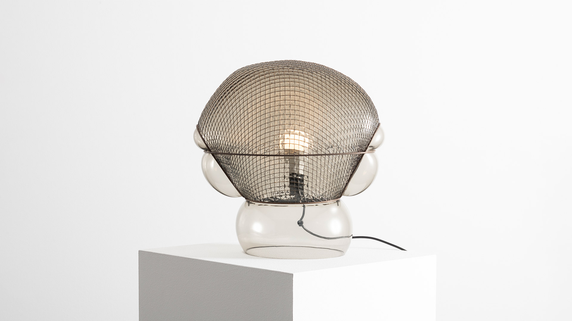 Artemide Patroclo table lamp: dome-shaped metal mesh shade over clear glass spherical base with visible Edison bulb