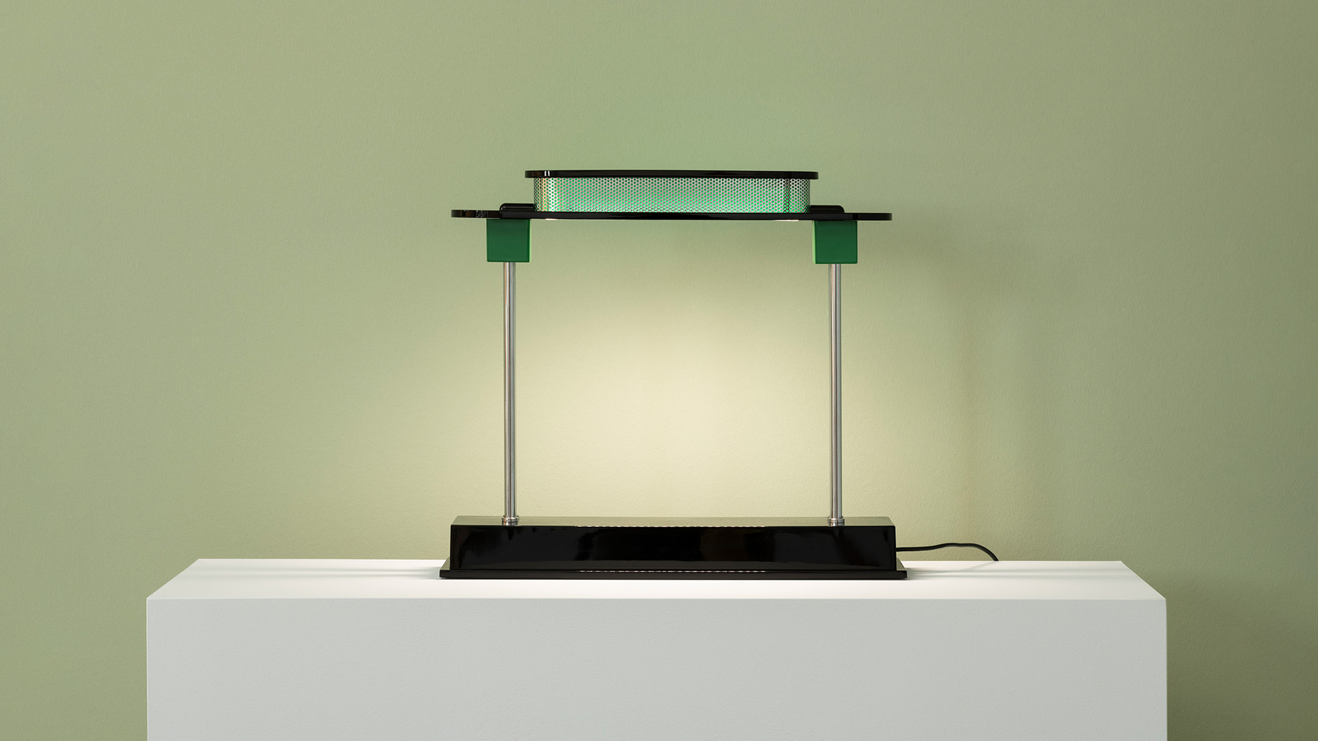 Close-up of Artemide Pausania lamp: dark perforated metal shade emitting vibrant green LED light through circular holes