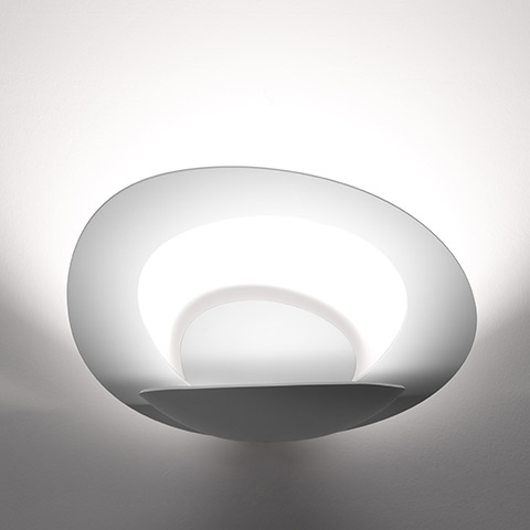 Artemide Pirce Parete wall lamp: white organic-shaped diffuser emitting soft upward and indirect light against a white wall