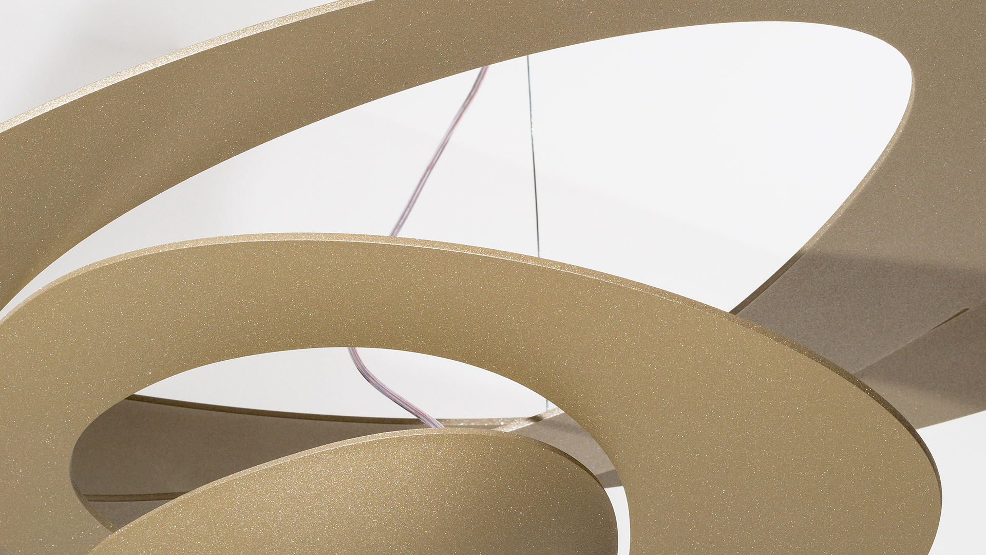 Artemide Pirce Sospensione pendant lamp with golden spiral rings emitting warm light, suspended against a teal paneled wall