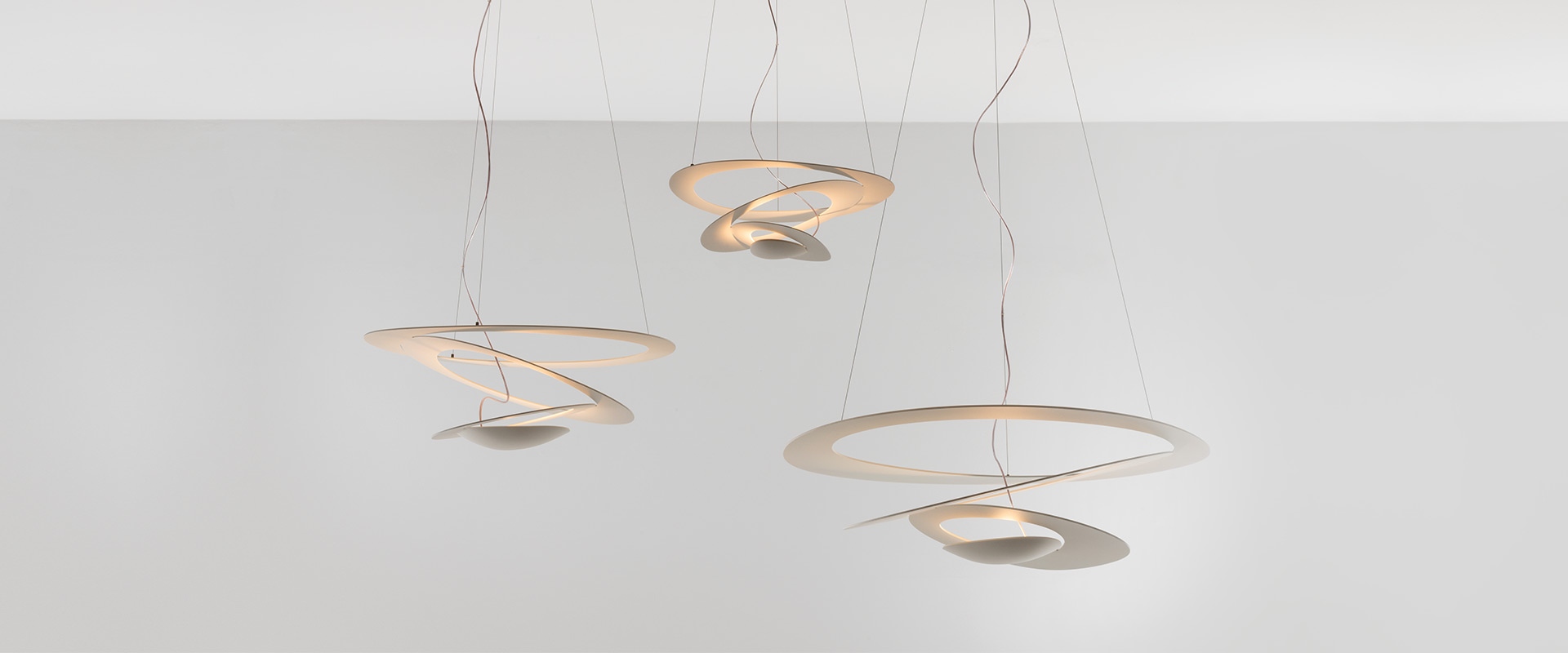 Artemide Pirce pendant lamp: white sculptural spiral shade with concentric rings emitting soft diffused light, suspended by thin cables