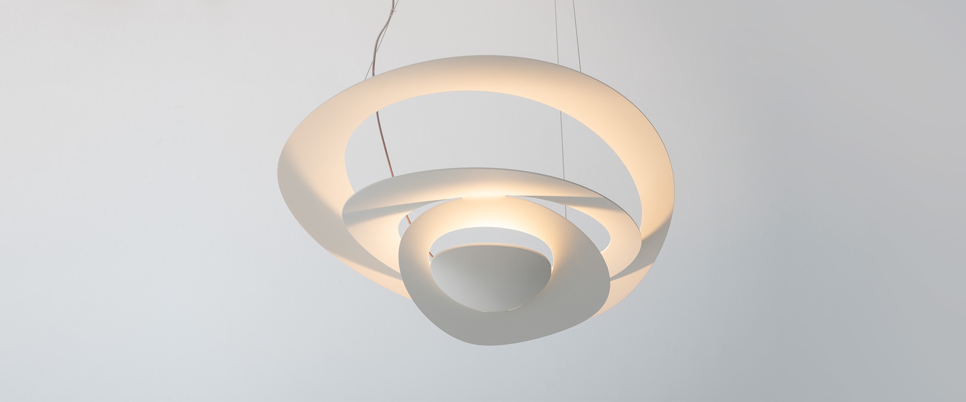 Artemide Pirce suspension lamp: sculptural interlocking spiral aluminum shades emitting warm golden light, hanging from thin cables