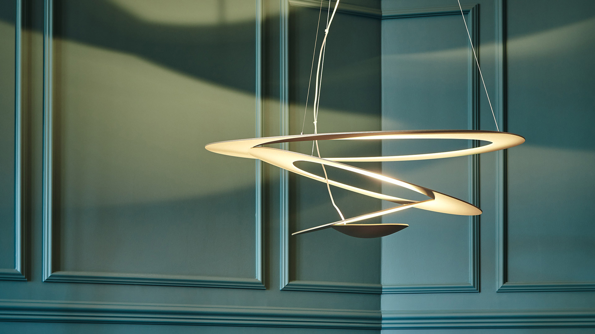 Close-up of Artemide Pirce Sospensione pendant lamp, featuring elegant overlapping spiral aluminum rings in warm gold finish