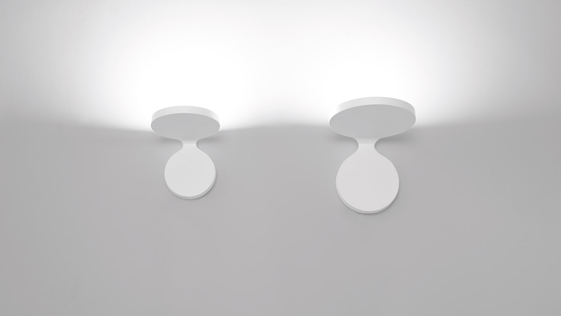 Two Artemide Rea wall/ceiling spotlights in white, featuring circular heads tilted downward, casting upward ambient light