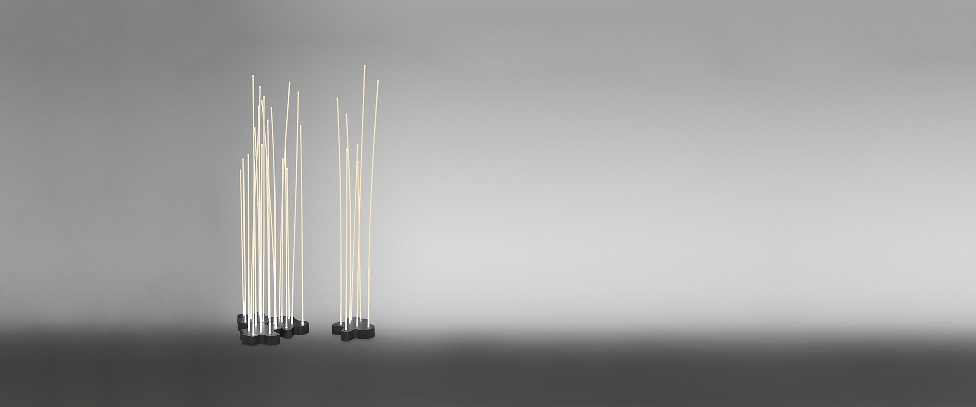 Artemide Reeds Outdoor luminaires arranged among garden plants at dusk, mimicking illuminated bamboo stems beside purple wildflowers
