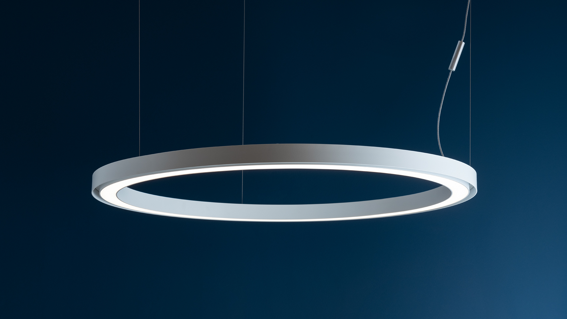 Artemide Ripple pendant lamps: four circular LED rings in grey, varying sizes, suspended above a dark table with a small vase