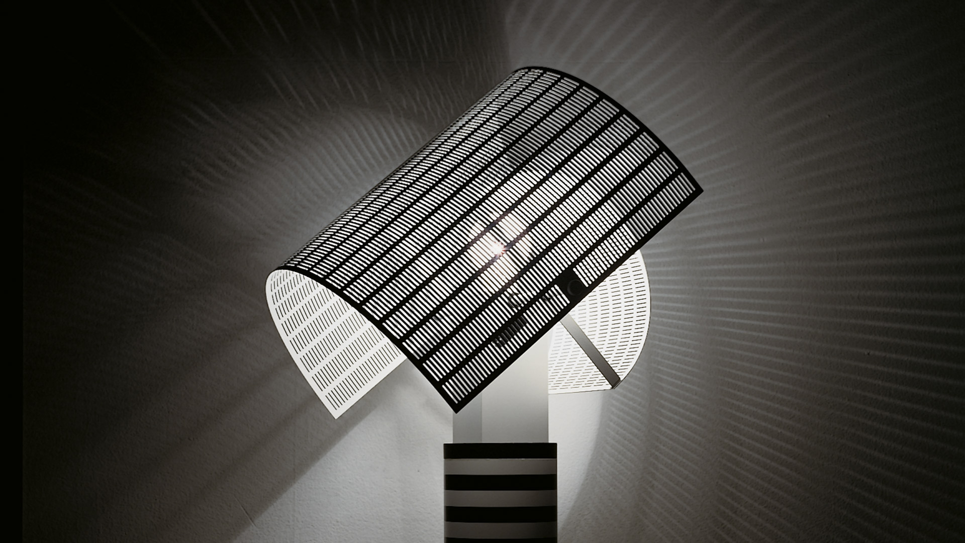 Modern living room with Artemide Shogun table lamp on desk, featuring striped base and white diffuser, beside a wall-mounted TV unit