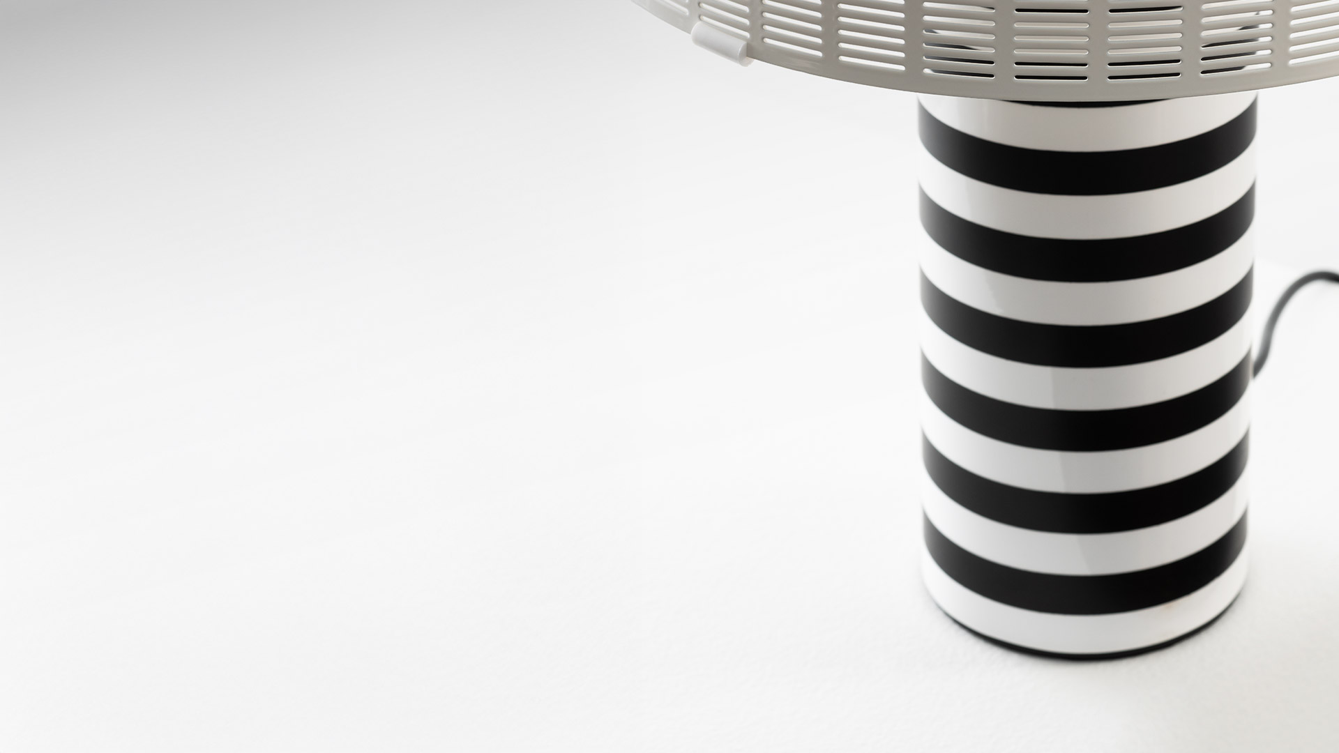 Artemide Shogun table lamp with semicircular slatted gold shade and black-and-white striped cylindrical base on a dark pedestal