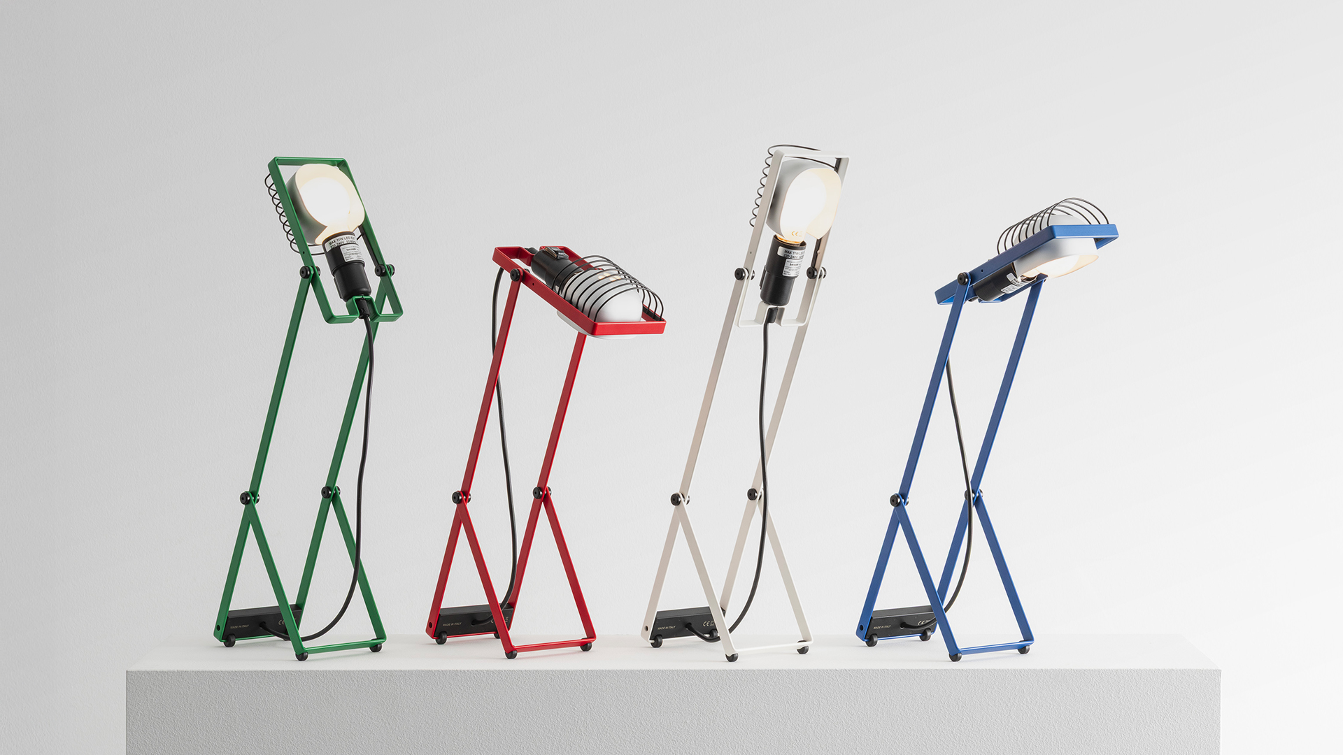 Two Artemide Sintesi wall lamps with scissor arms: red one with striped shade below, green one with bare bulb above