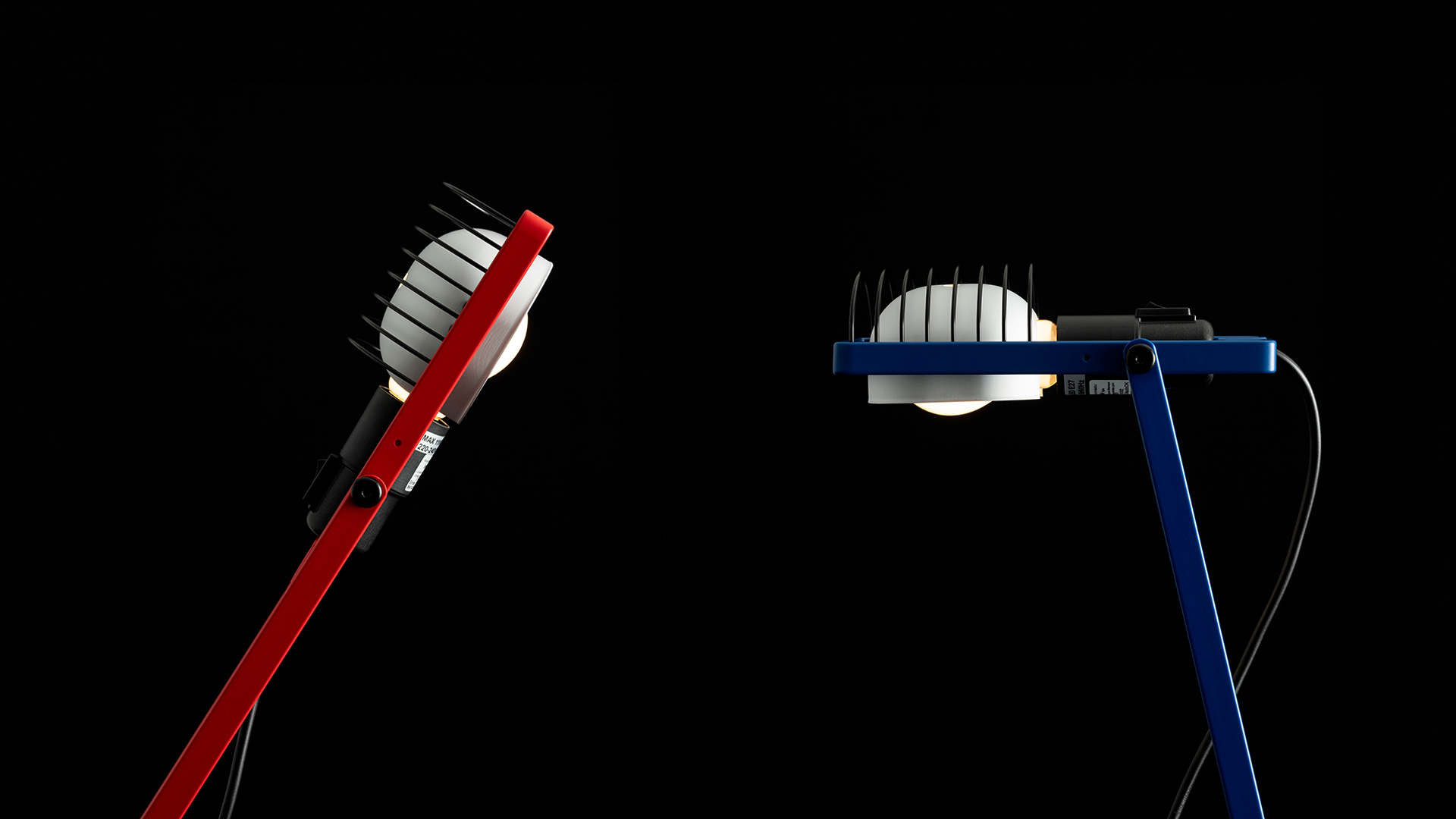 Sintesi desk lamp in blue with articulated arm and caged LED head, mounted on white base, illuminating an open book on a white desk