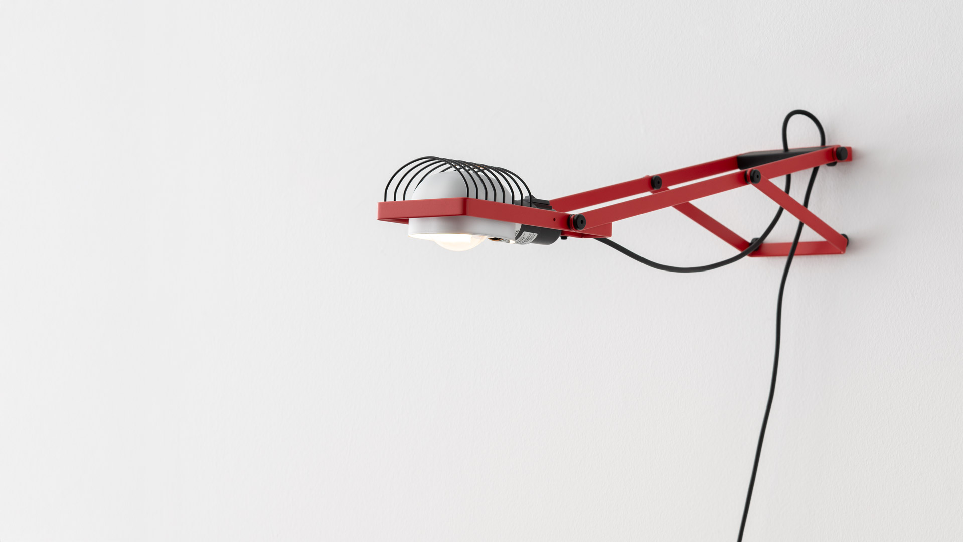 Four Artemide Sintesi table lamps with wire frames in green, red, clear, and blue, each with a louvered white shade and black cord